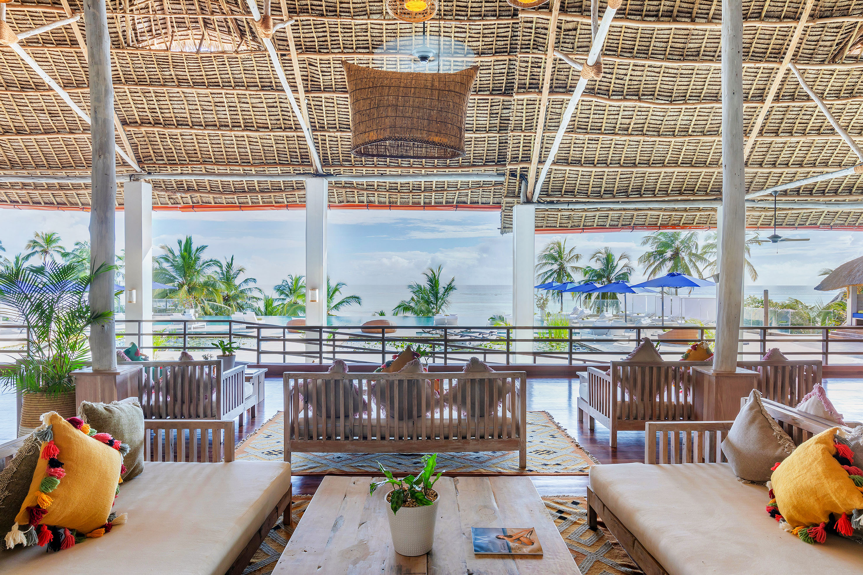 Tropical resort lounge with ocean view, thatch roof, and palm trees.