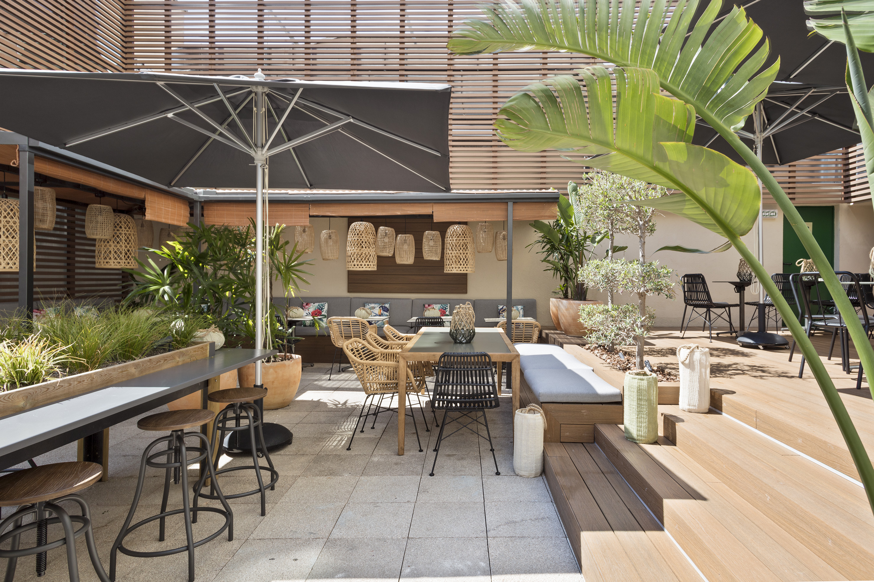 Shaded outdoor patio with rattan seating, dining tables, and tropical plants.