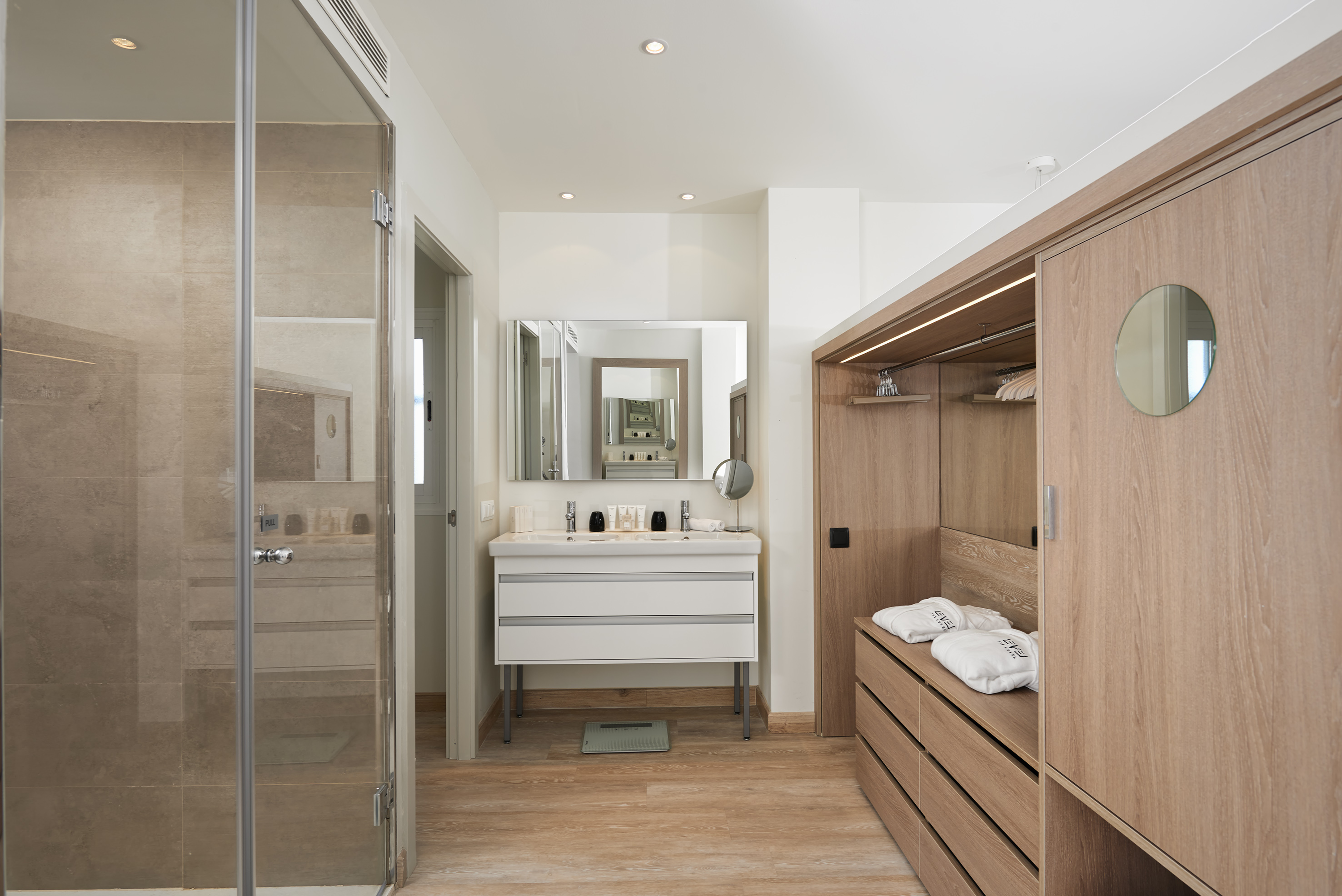Modern bathroom with glass shower, double vanity, and integrated wooden closet.