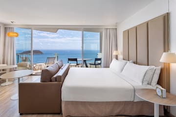 a room with a large bed and a table and chairs overlooking the ocean