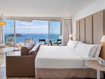 a room with a large bed and a table and chairs overlooking the ocean