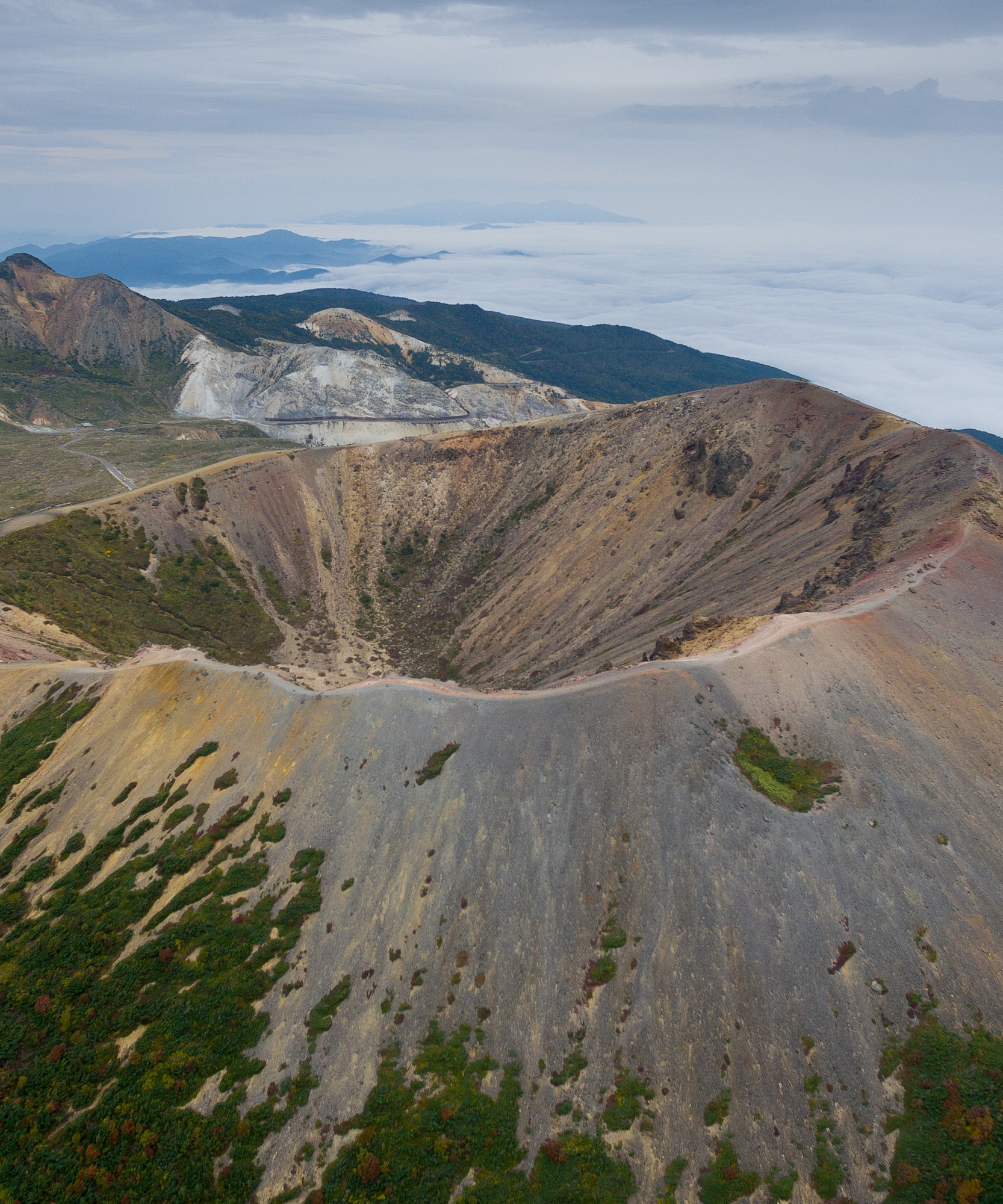 Cráter volcánico desde el aire, montañas, mar de nubes y vegetación otoñal.