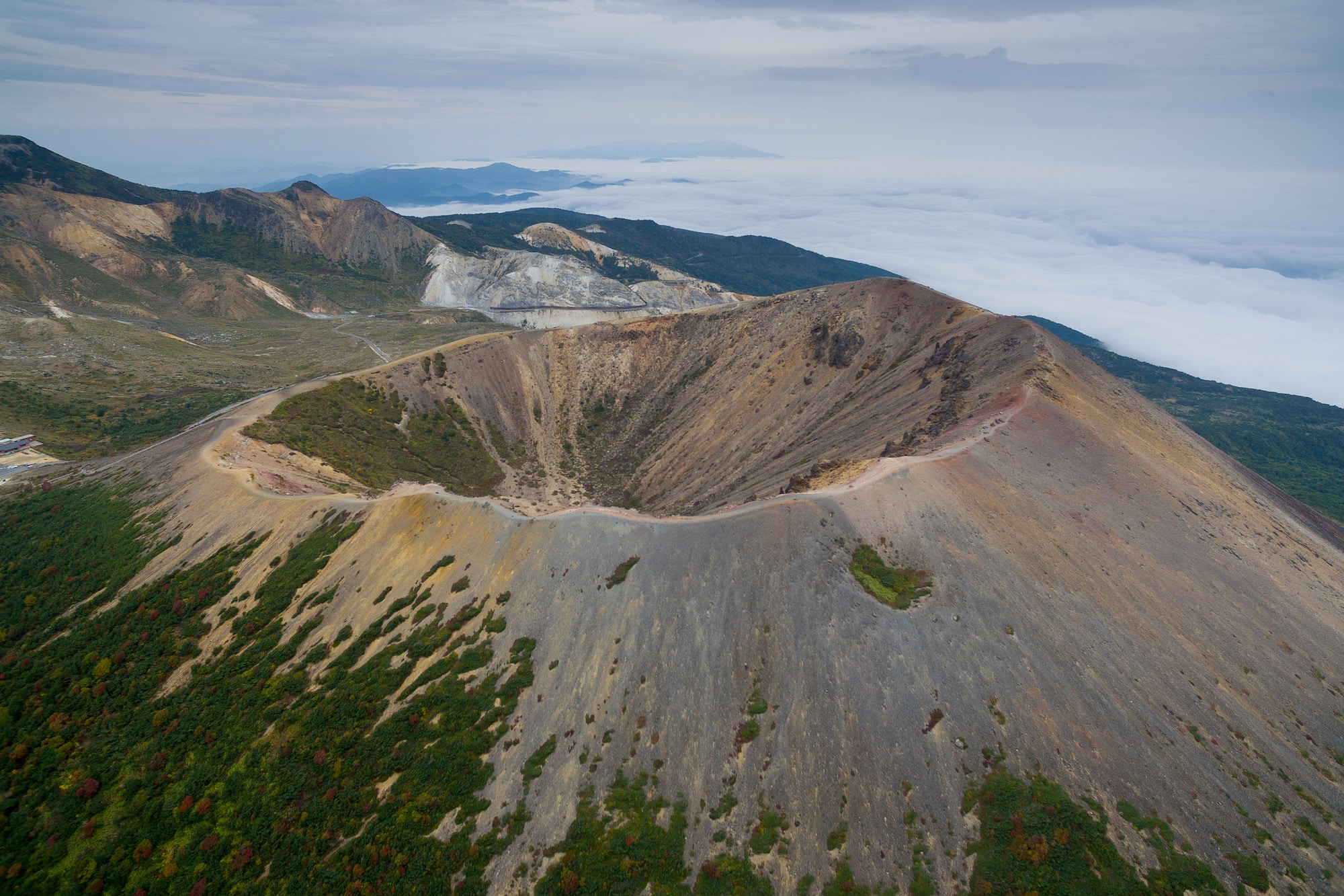 Cráter volcánico, montañas, vegetación otoñal y mar de nubes. Vista aérea.