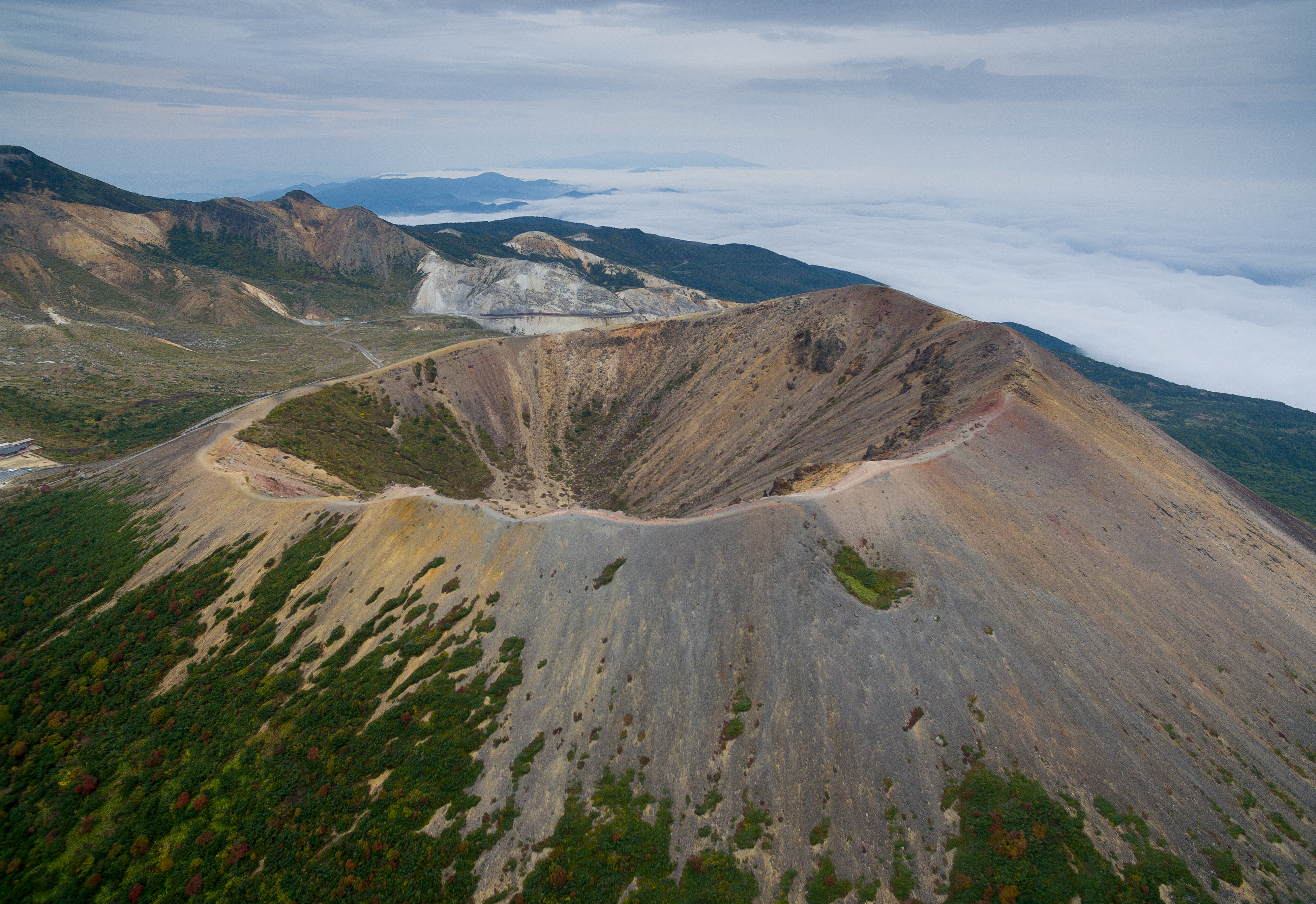 Cráter volcánico, montañas, vegetación otoñal y mar de nubes. Vista aérea.