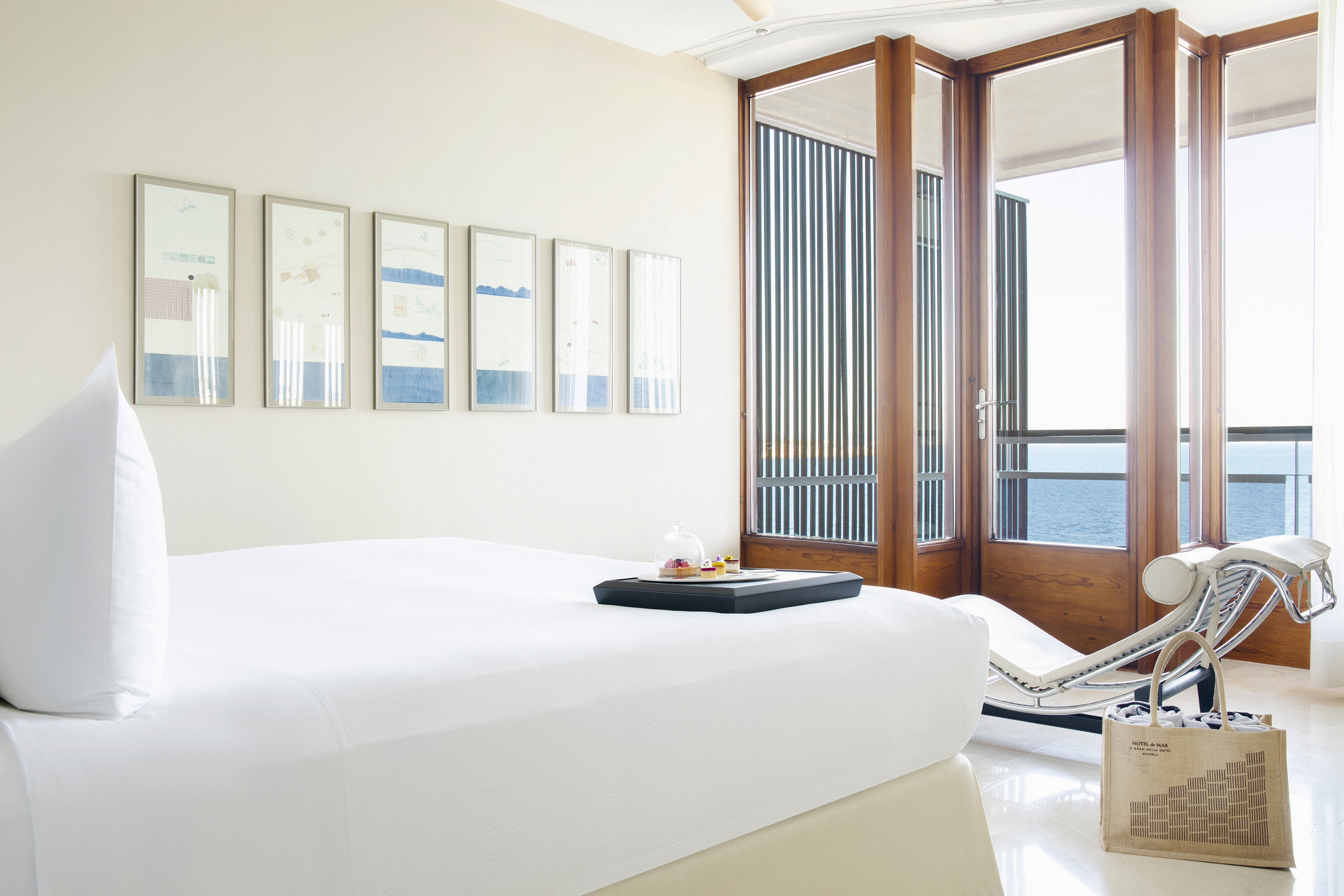 Ocean view hotel bedroom with white bed and modern sliding glass doors.