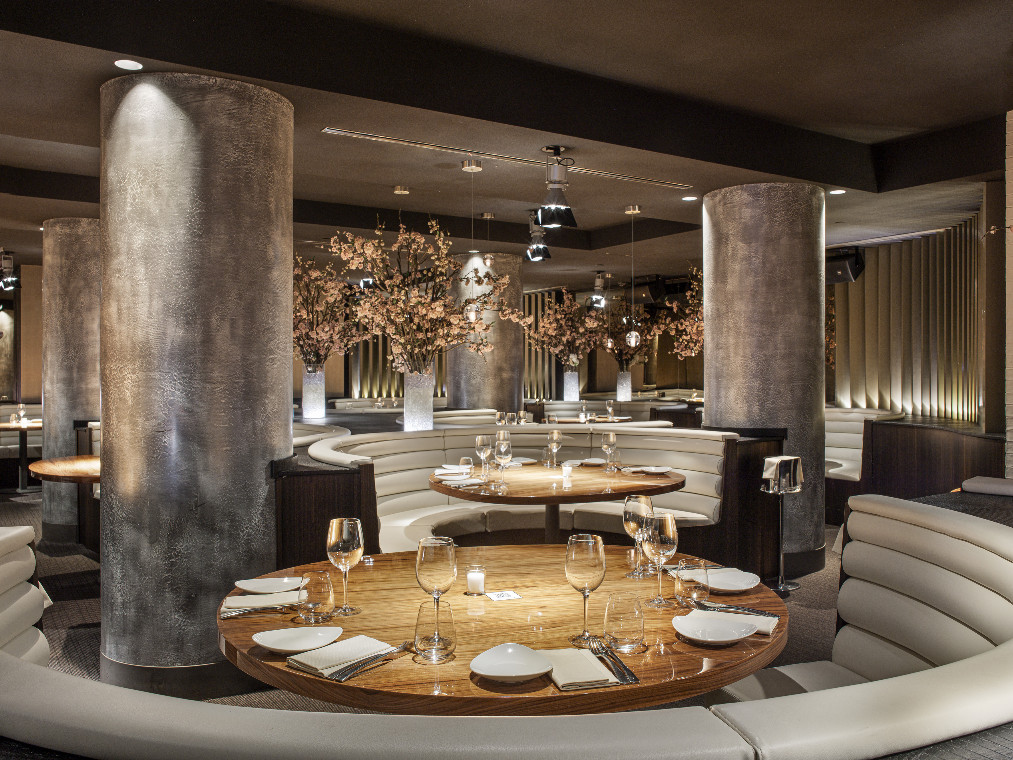 Upscale restaurant interior with round tables, white booths, and cherry blossom decor.