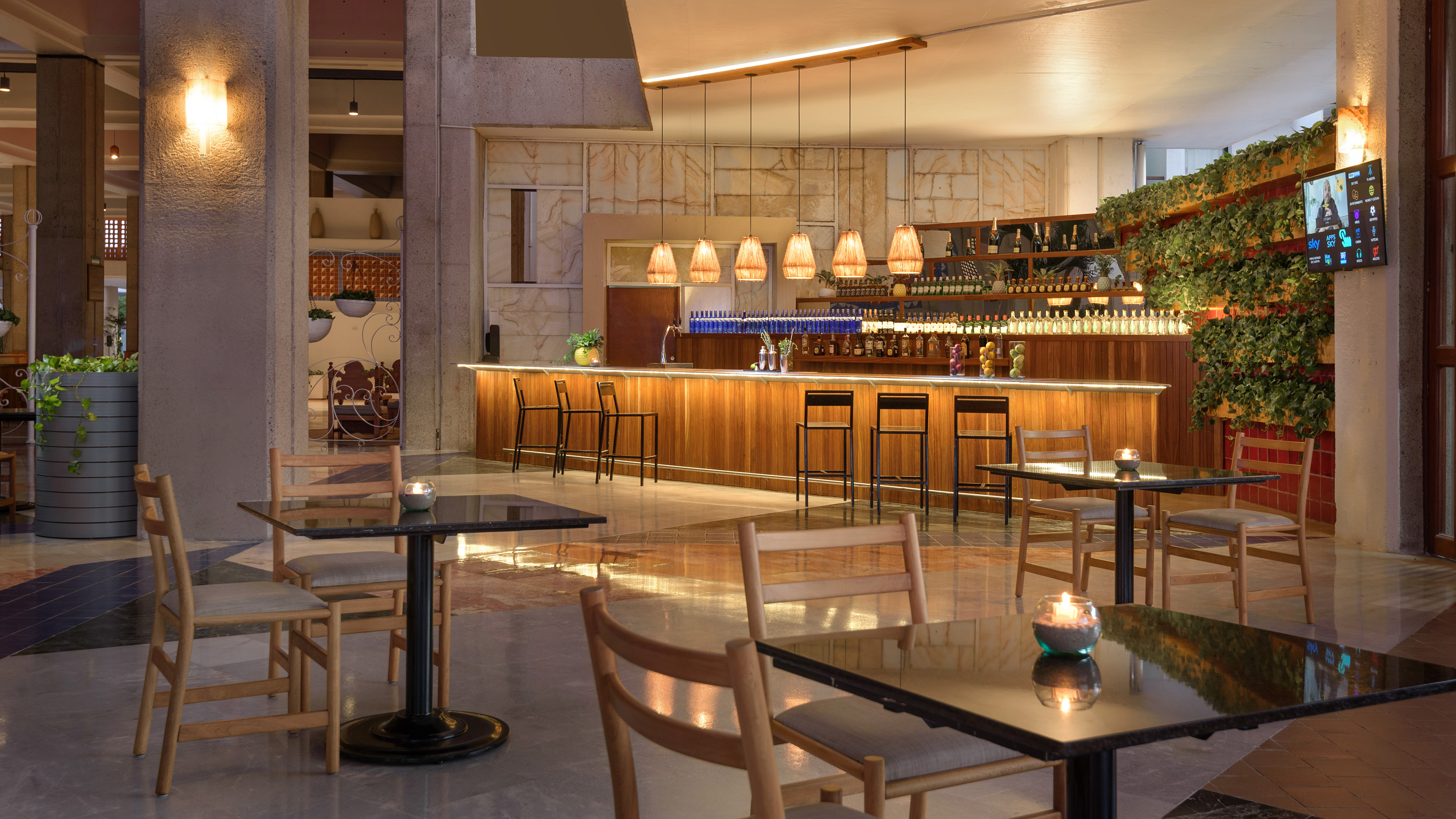 Modern hotel bar with wooden counter, stools, warm lighting, and green wall.