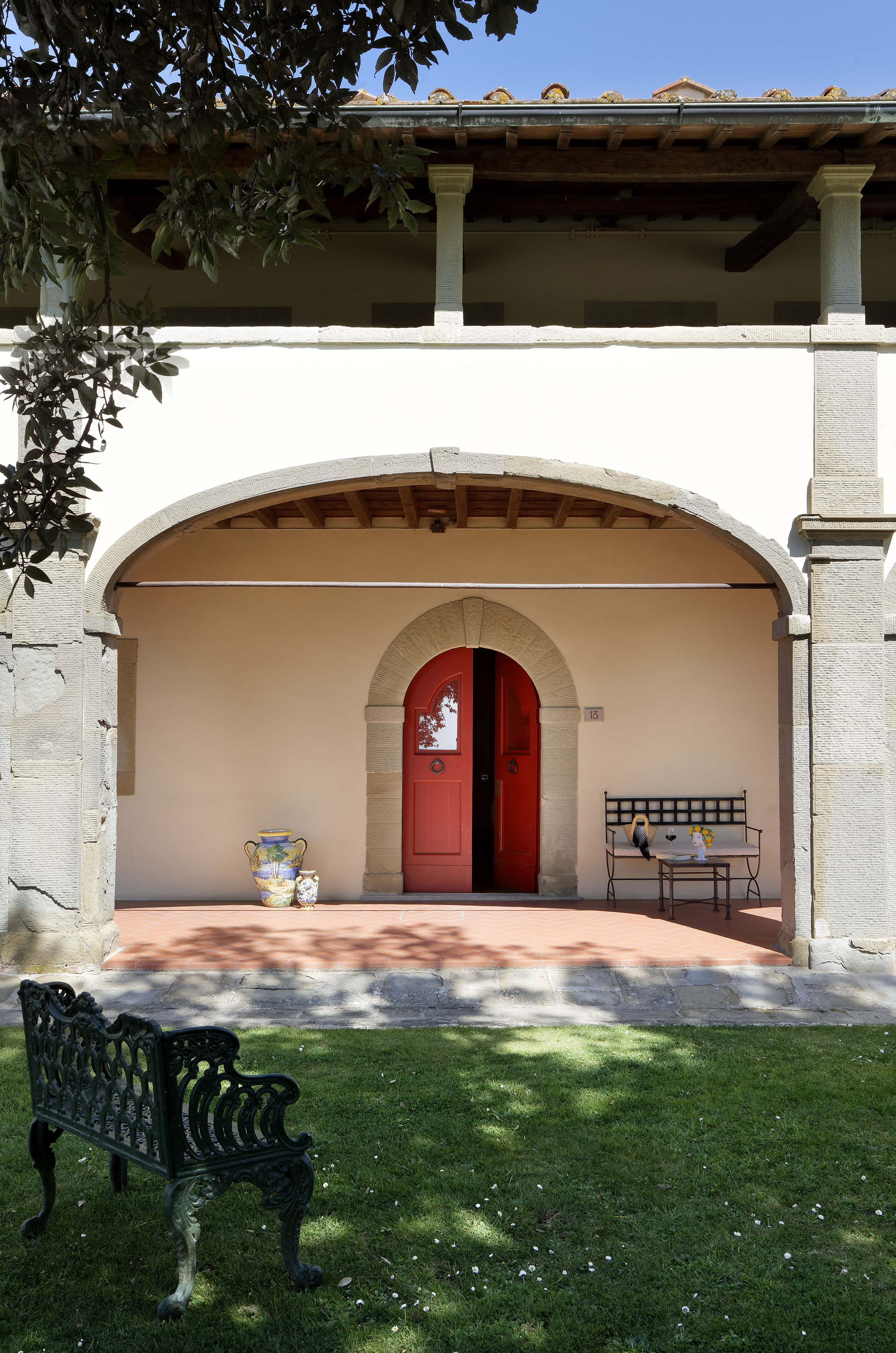 Tuscan villa patio with arched red door, garden bench, and terracotta floor.