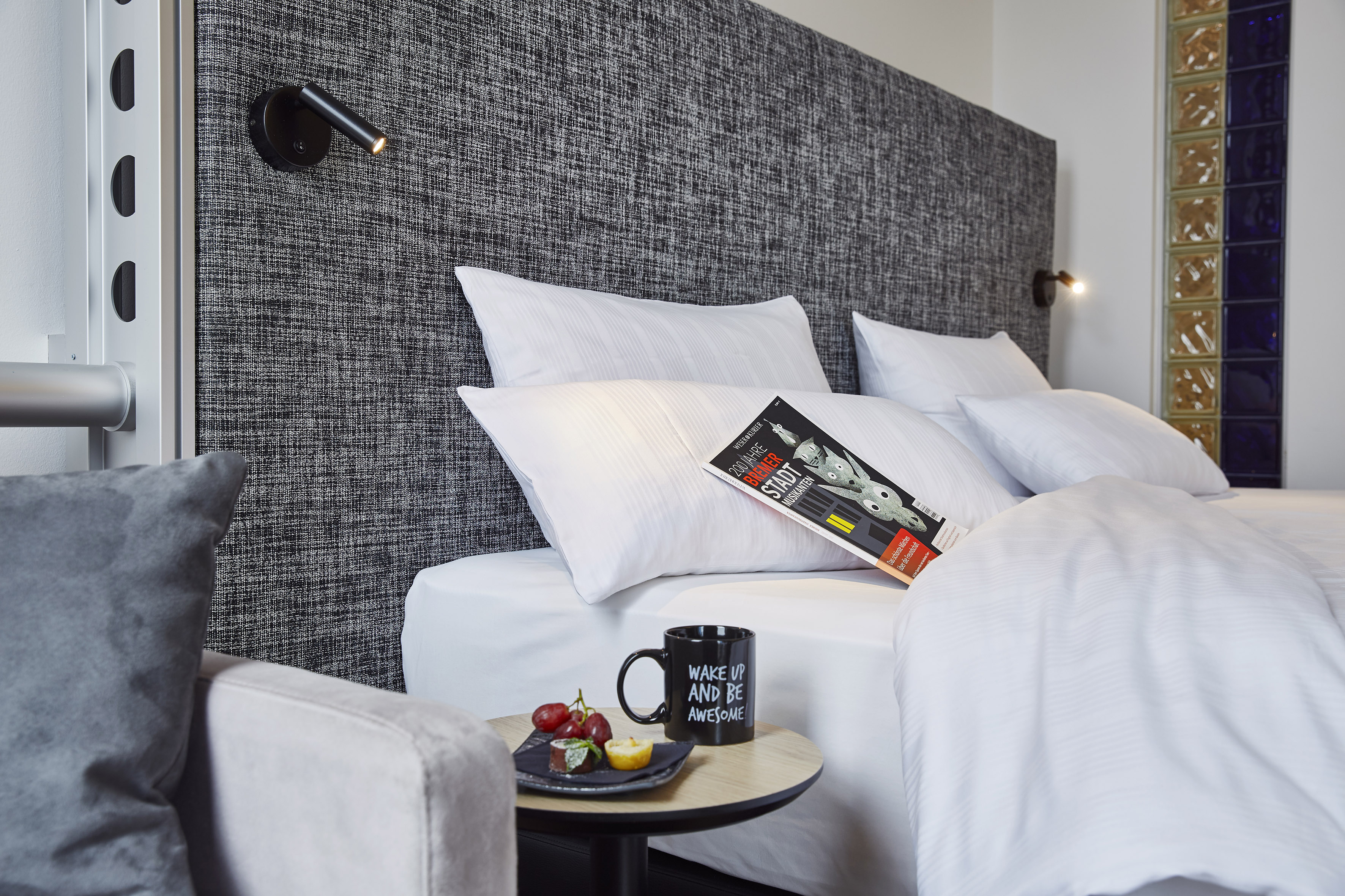 Habitación de hotel moderna con cama, cabecero texturizado, mesa de noche y refrigerios.