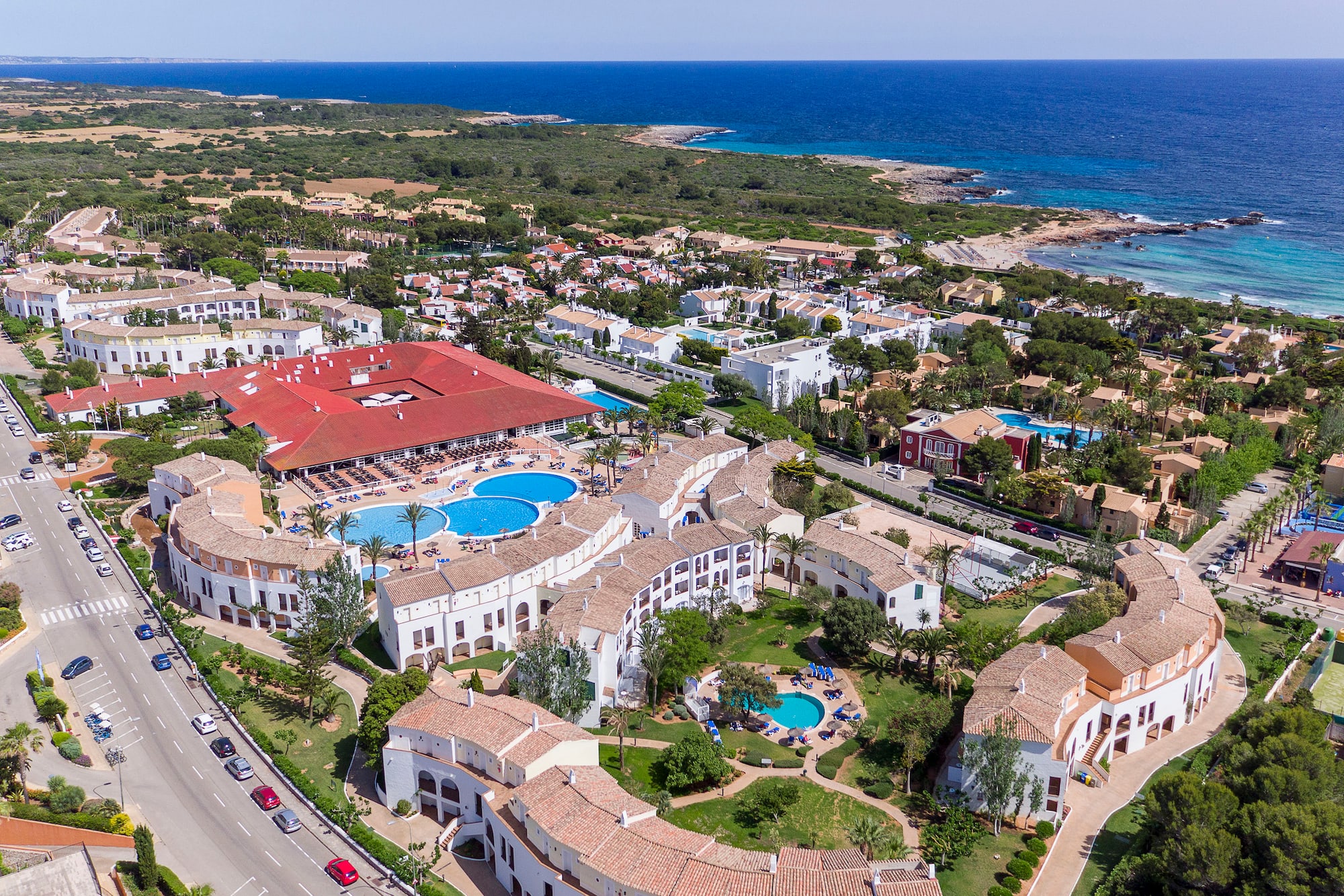 Aerial view of a coastal resort complex with pools, white buildings, and ocean.