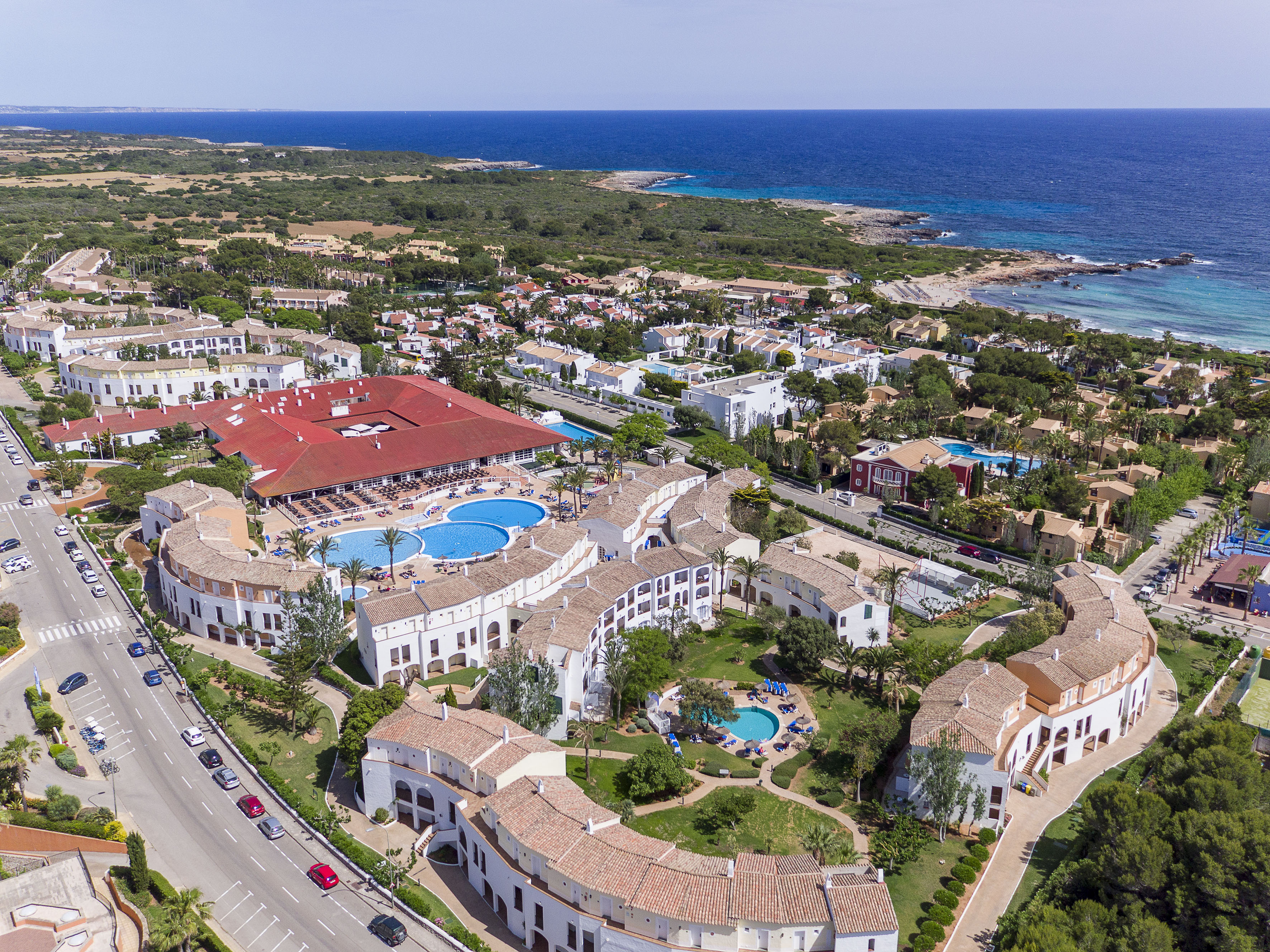 Aerial view of a coastal resort complex with pools, white buildings, and ocean.