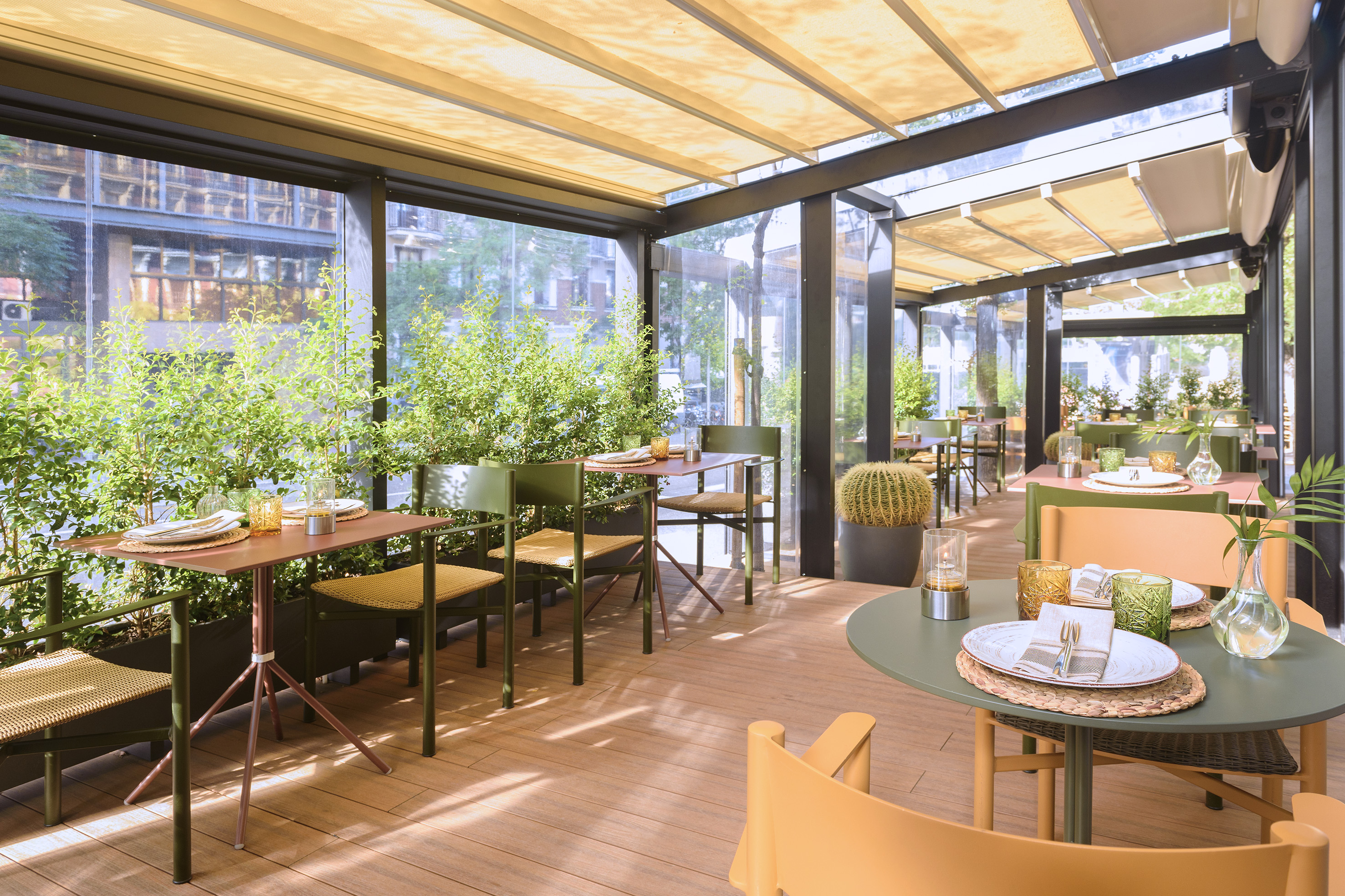 Modern outdoor restaurant patio with retractable roof, green plants, and dining tables.