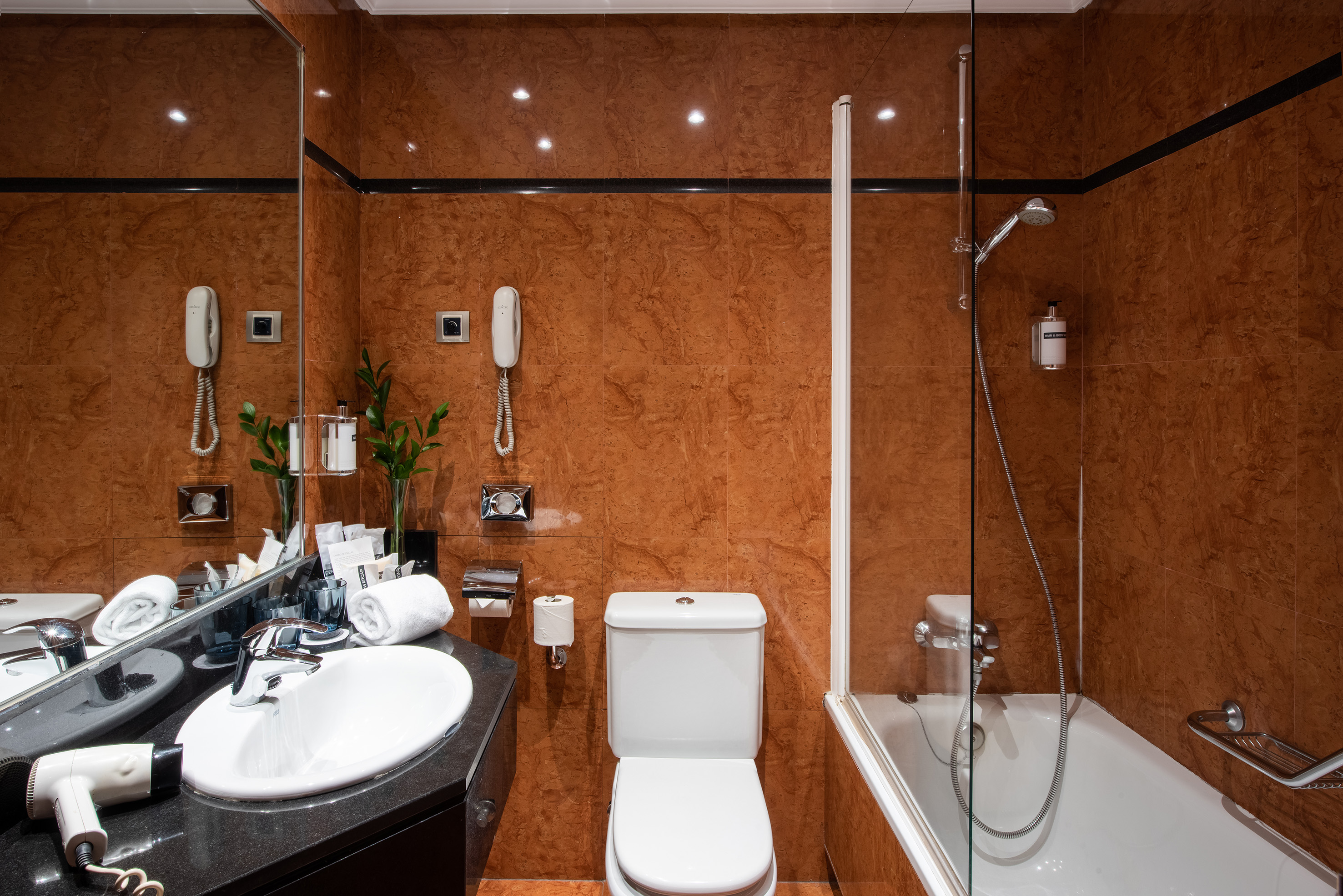 Brown tiled hotel bathroom with sink, toilet, and bathtub with shower.