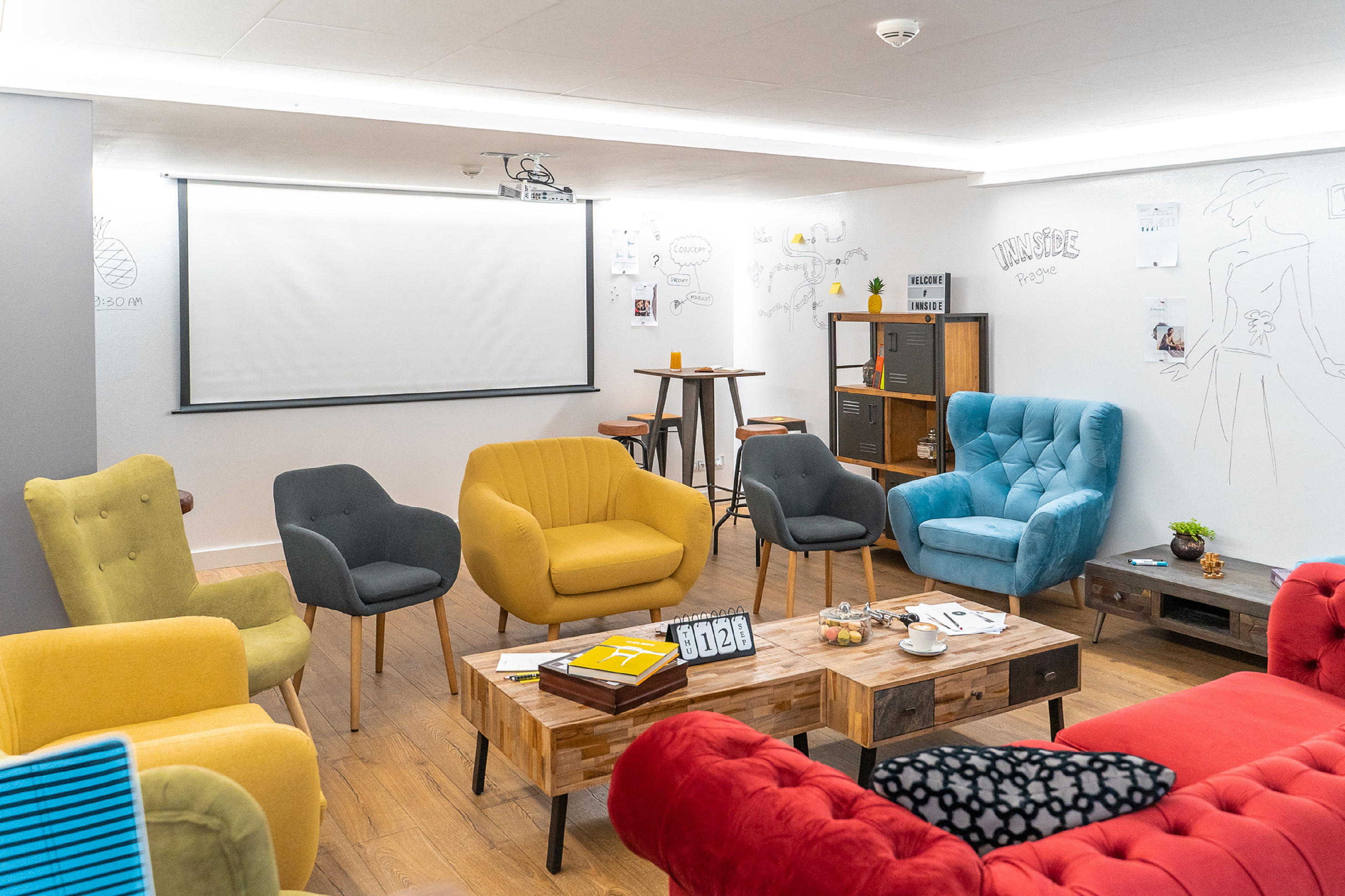 Colorful meeting lounge with projector screen and whiteboard sketches.