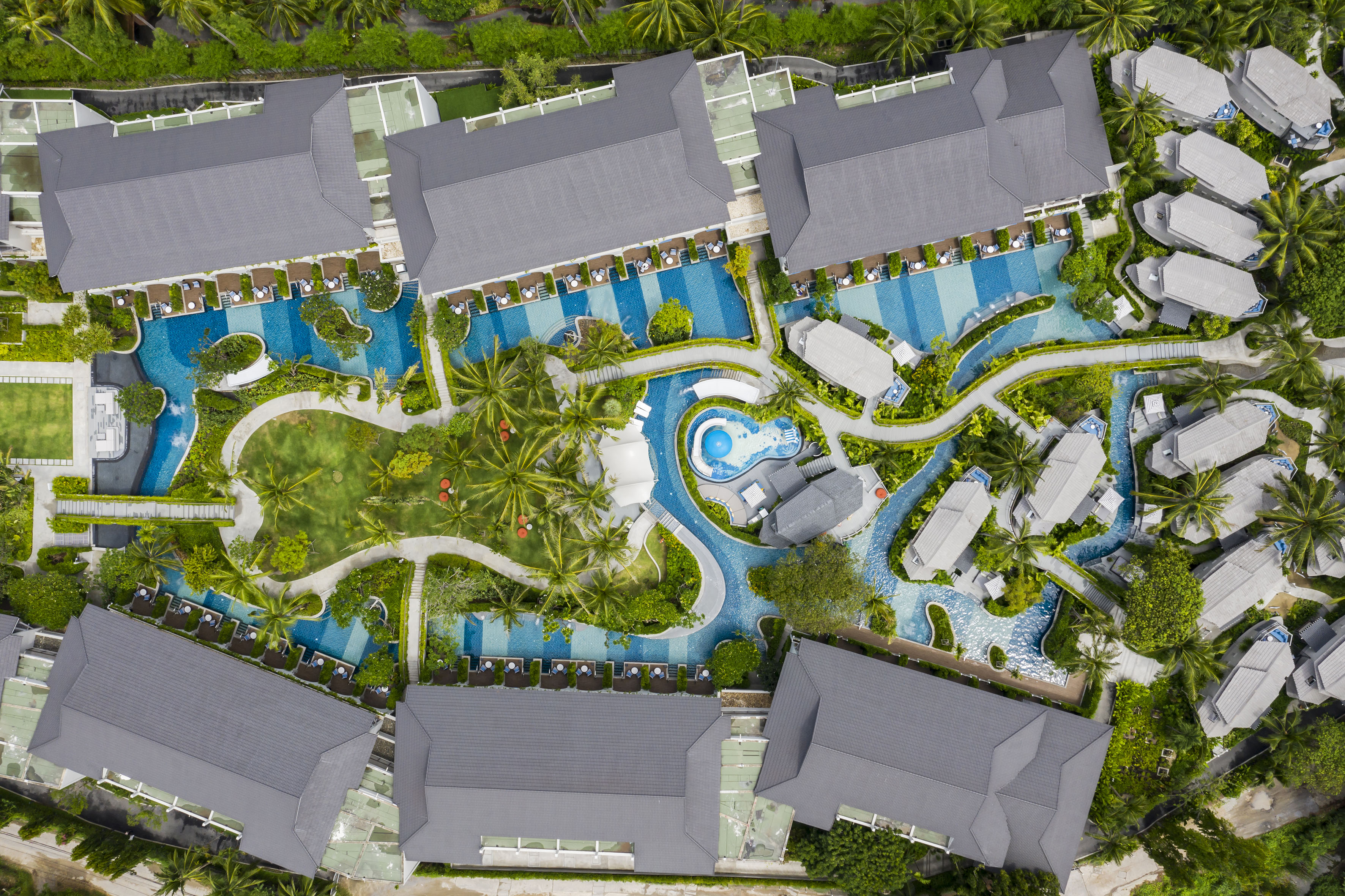Aerial view: tropical luxury resort with winding pools, villas, and palm trees.
