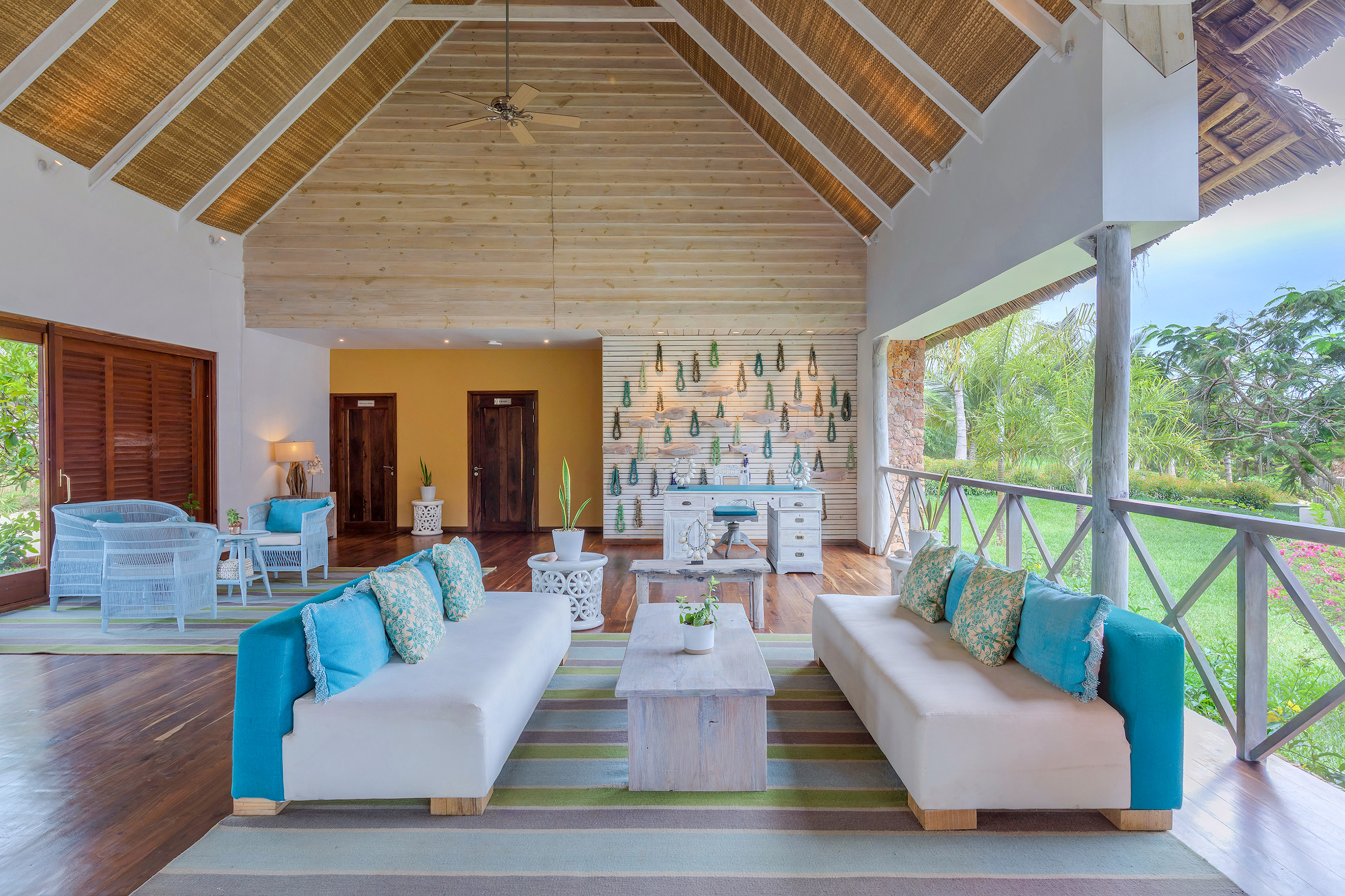 Tropical open-air lounge with thatched ceiling, white sofas, and garden view.