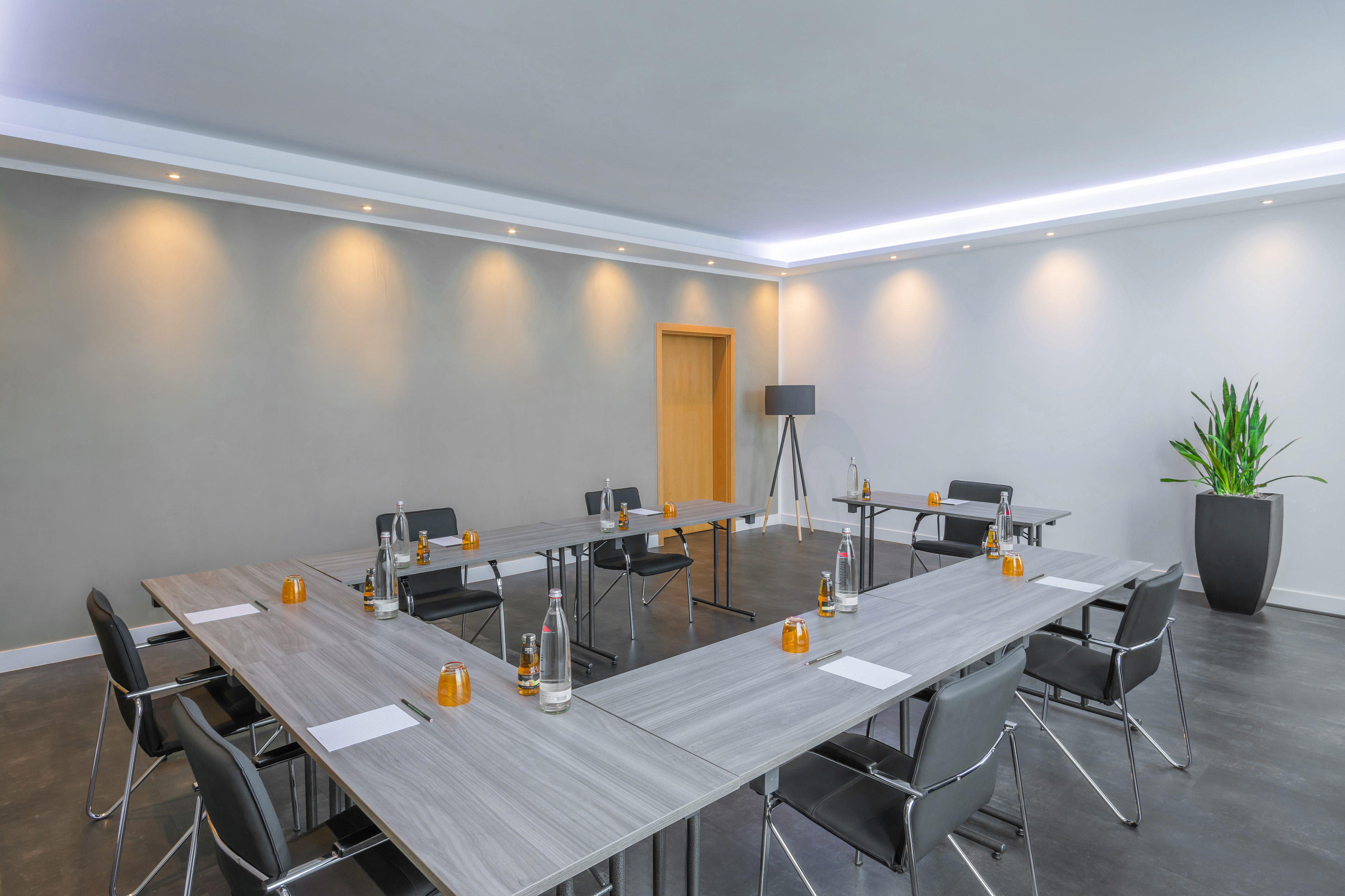 Modern business meeting room with U-shaped grey tables and black chairs.