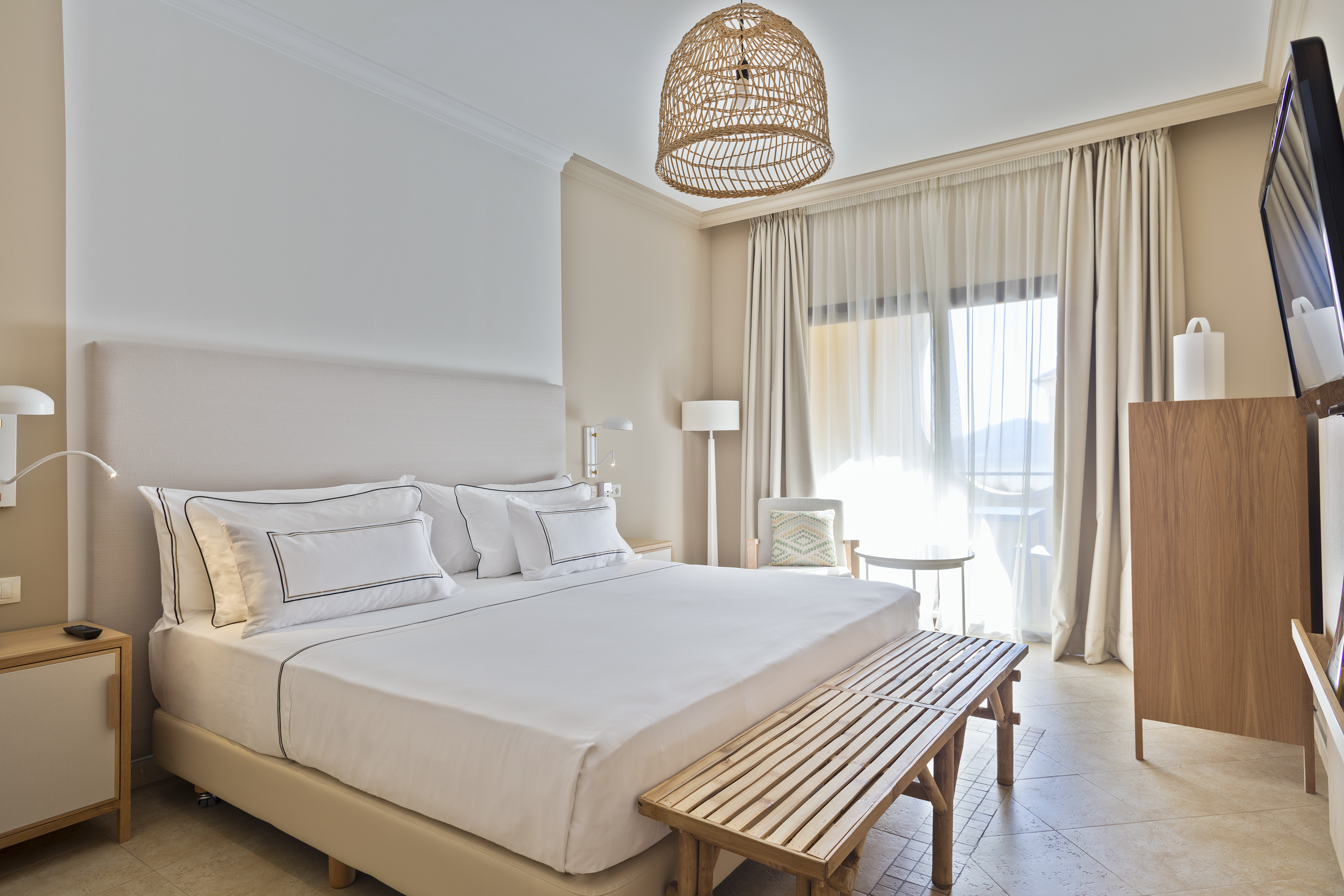 Bright, modern hotel bedroom with king bed, balcony, and woven pendant light.