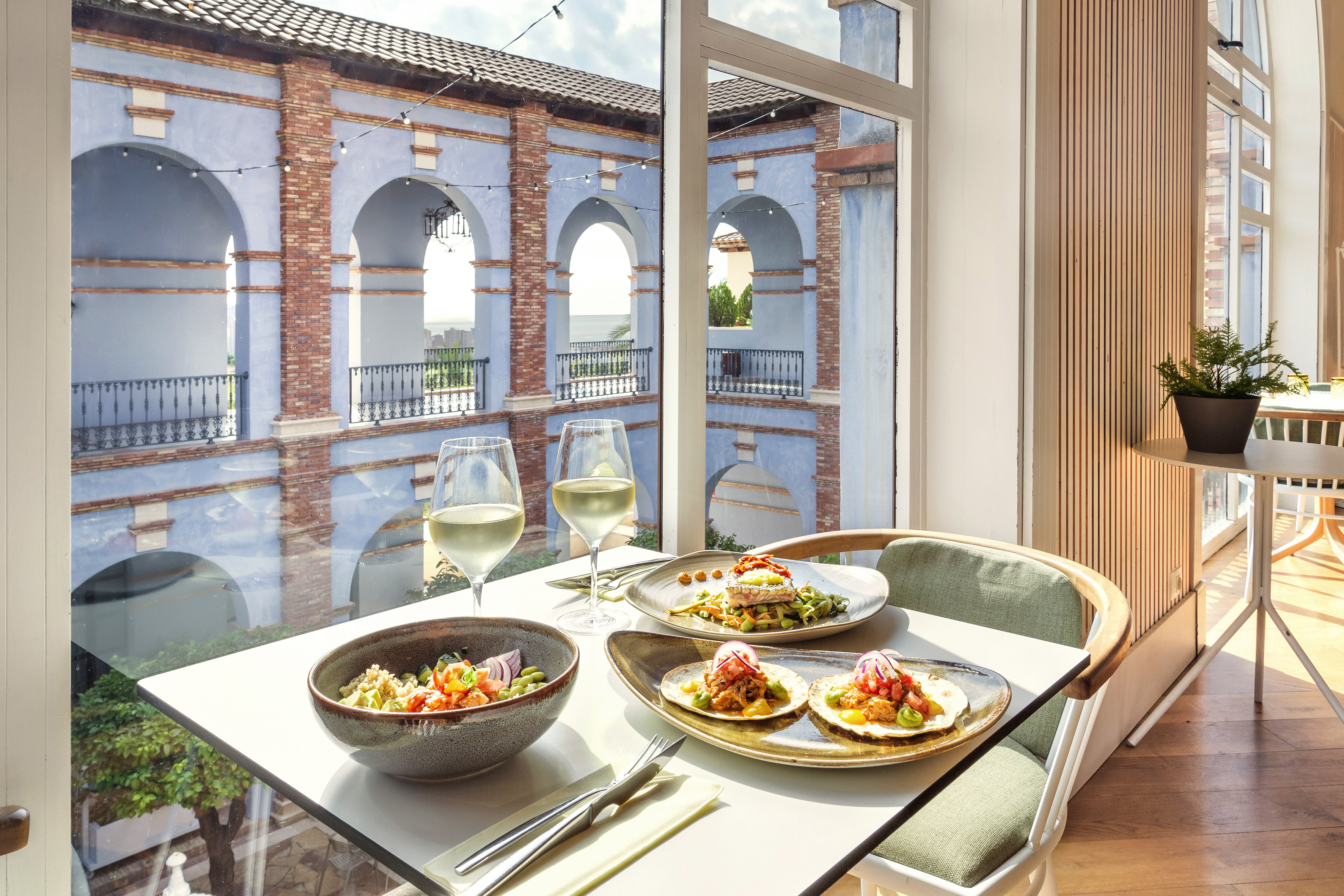 Dining table with tacos, salad, white wine, and a view of blue arched buildings.