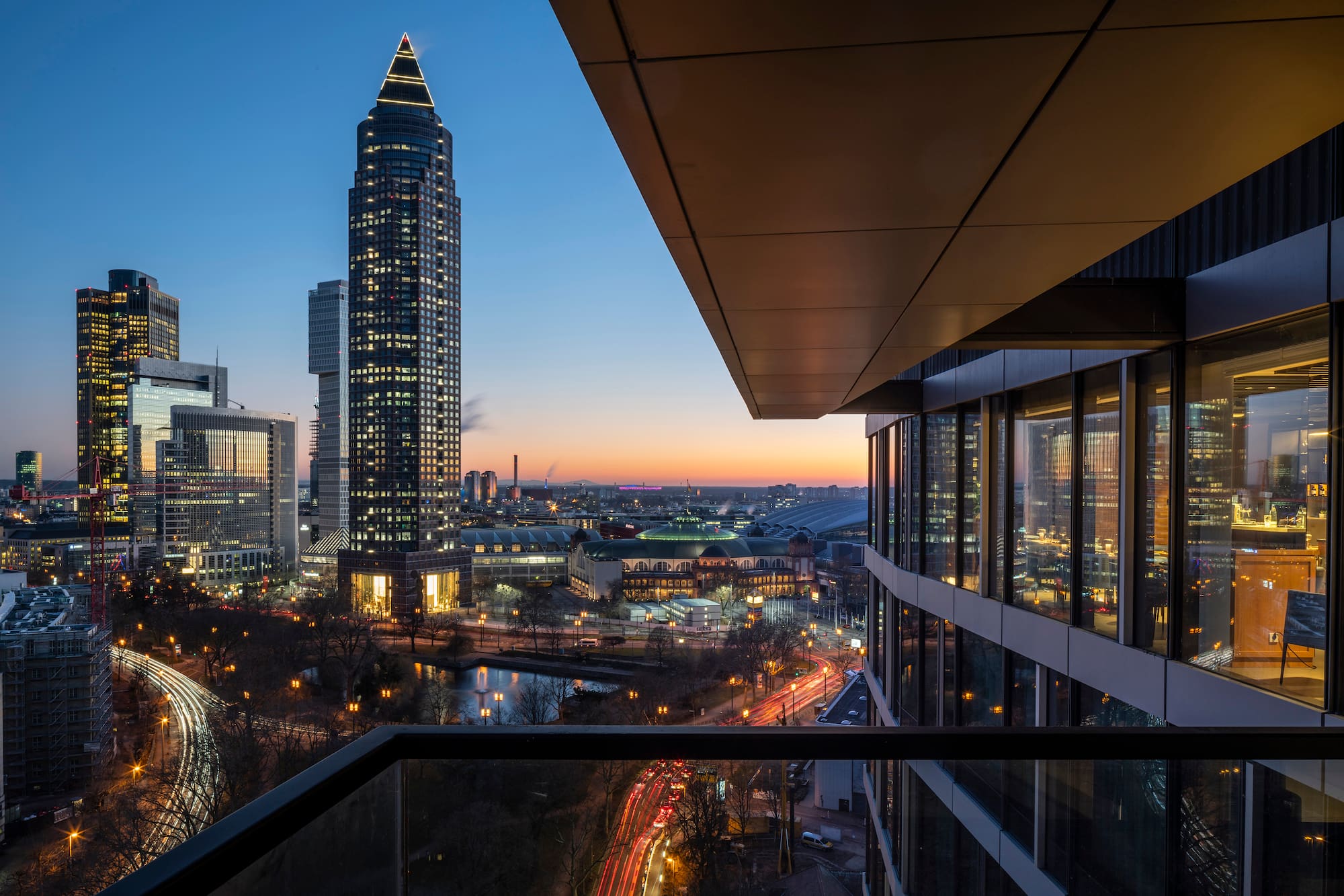 Frankfurt skyline at twilight with Messeturm, illuminated buildings, and car trails.