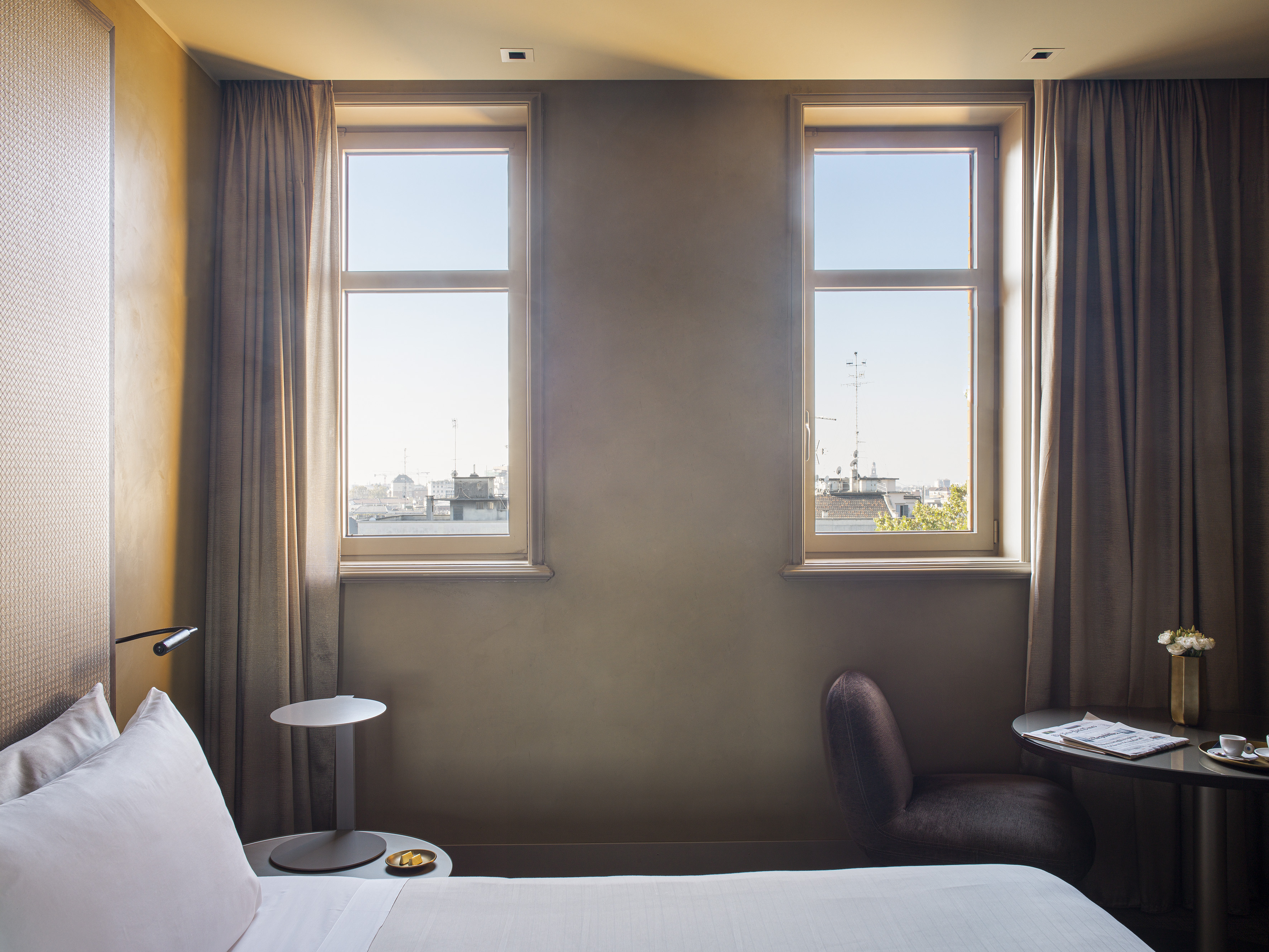 Modern hotel room with two windows, city view, bed, and cozy seating area.