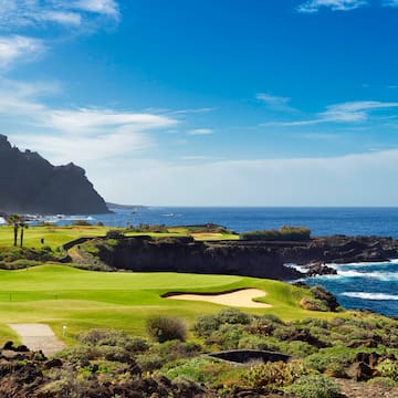 a golf course with a body of water and a hill