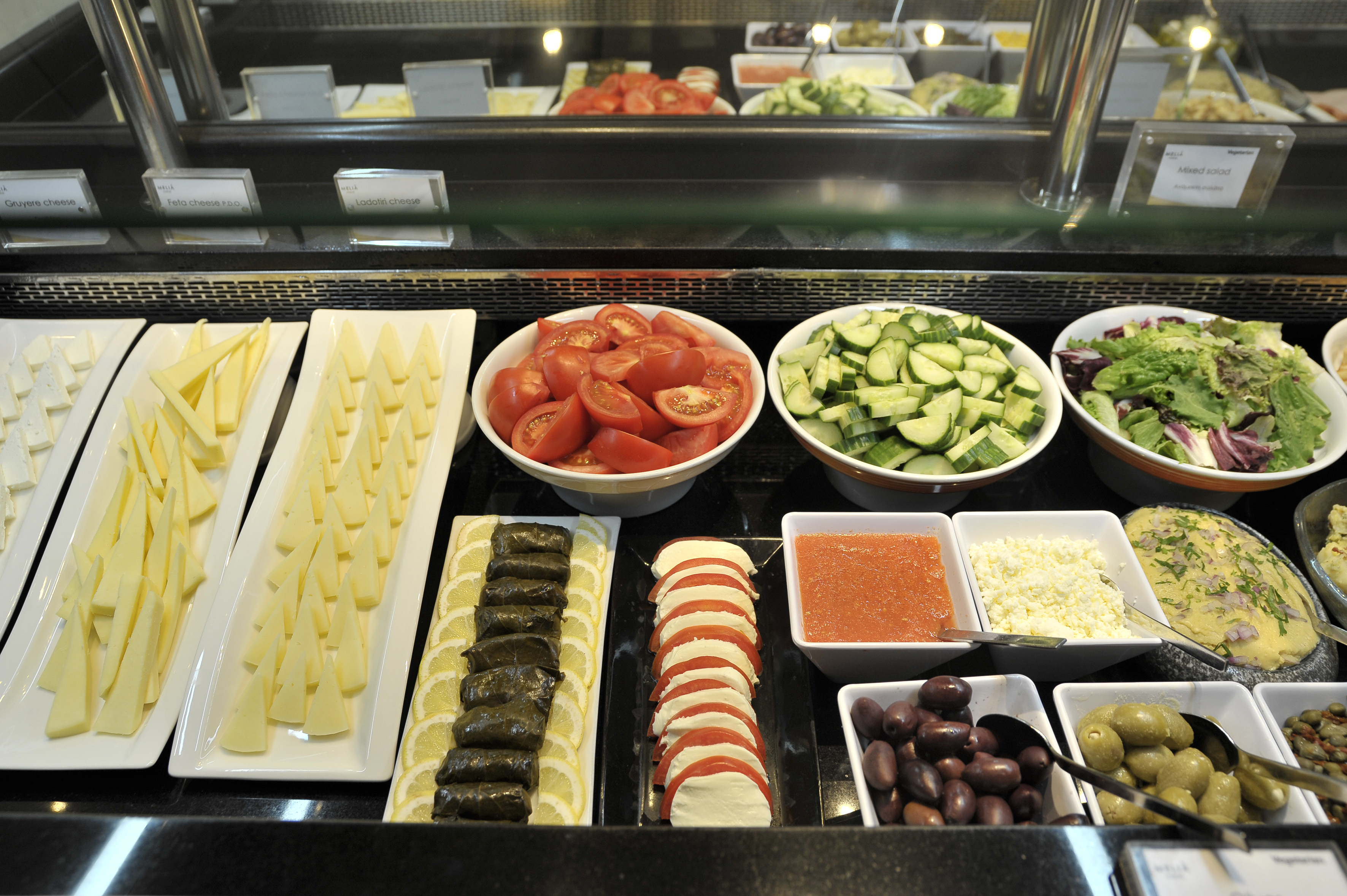 Fresh hotel buffet with various cheeses, vegetables, olives, and salads.