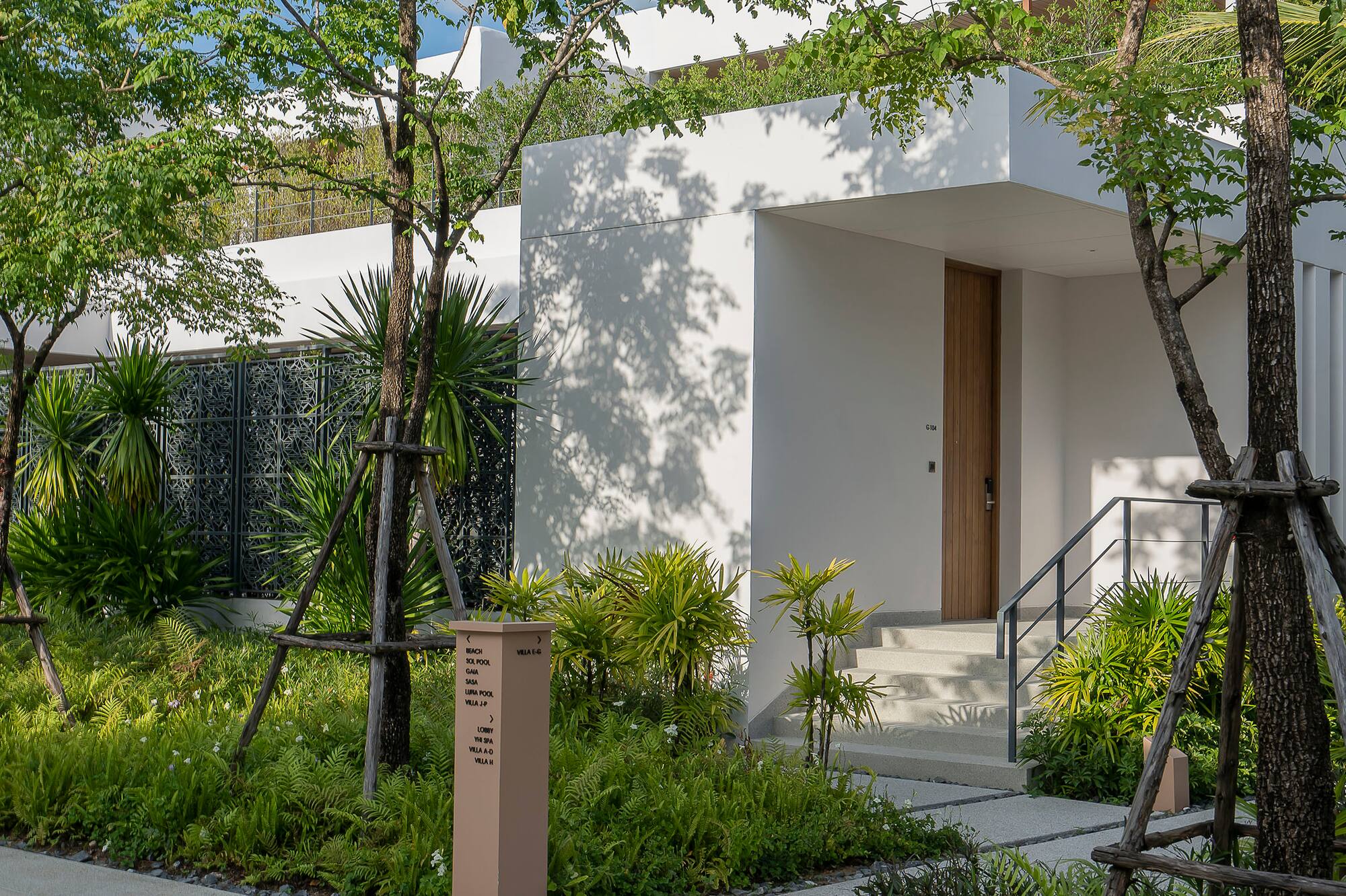 Modern resort villa entrance with lush tropical landscaping and pathway.