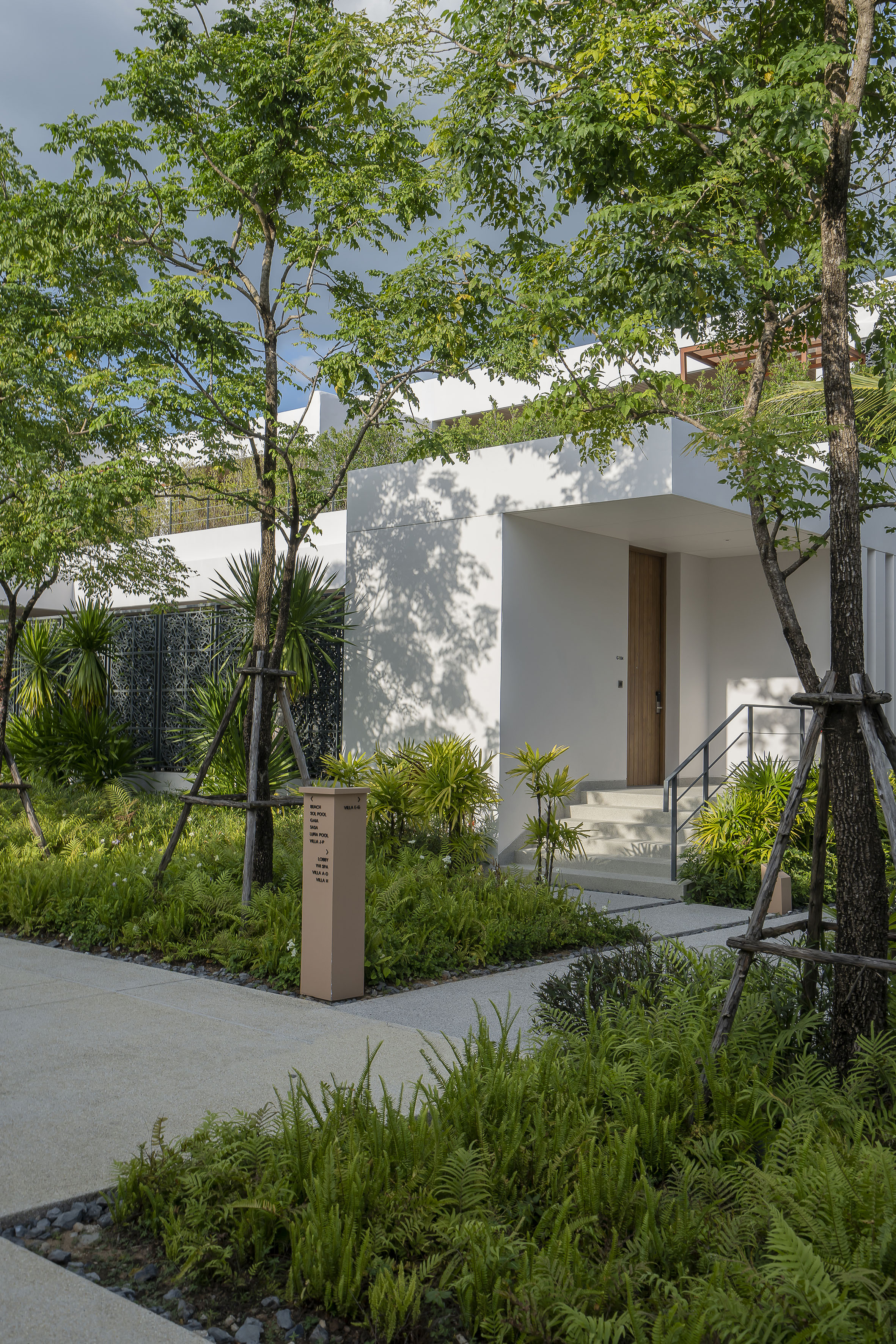 Modern resort villa entrance with lush tropical landscaping and pathway.