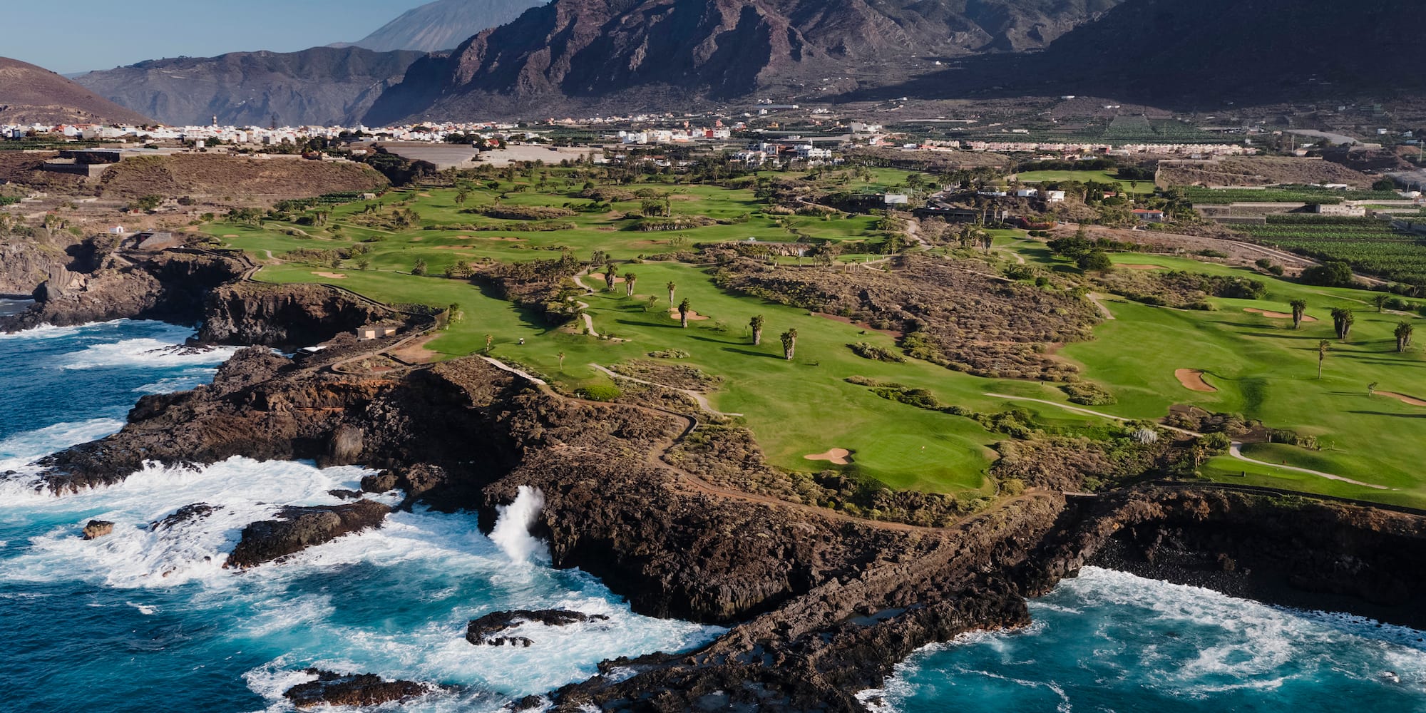 a golf course with a body of water and mountains in the background