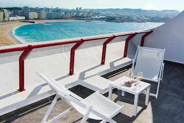 a white chairs and a table on a balcony overlooking a beach