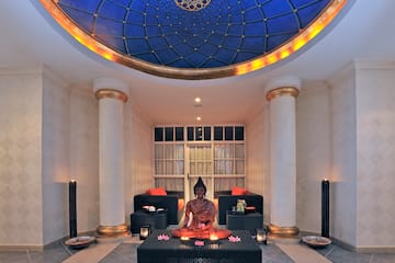 a statue of a buddha sitting on a table in a room with columns and blue ceiling