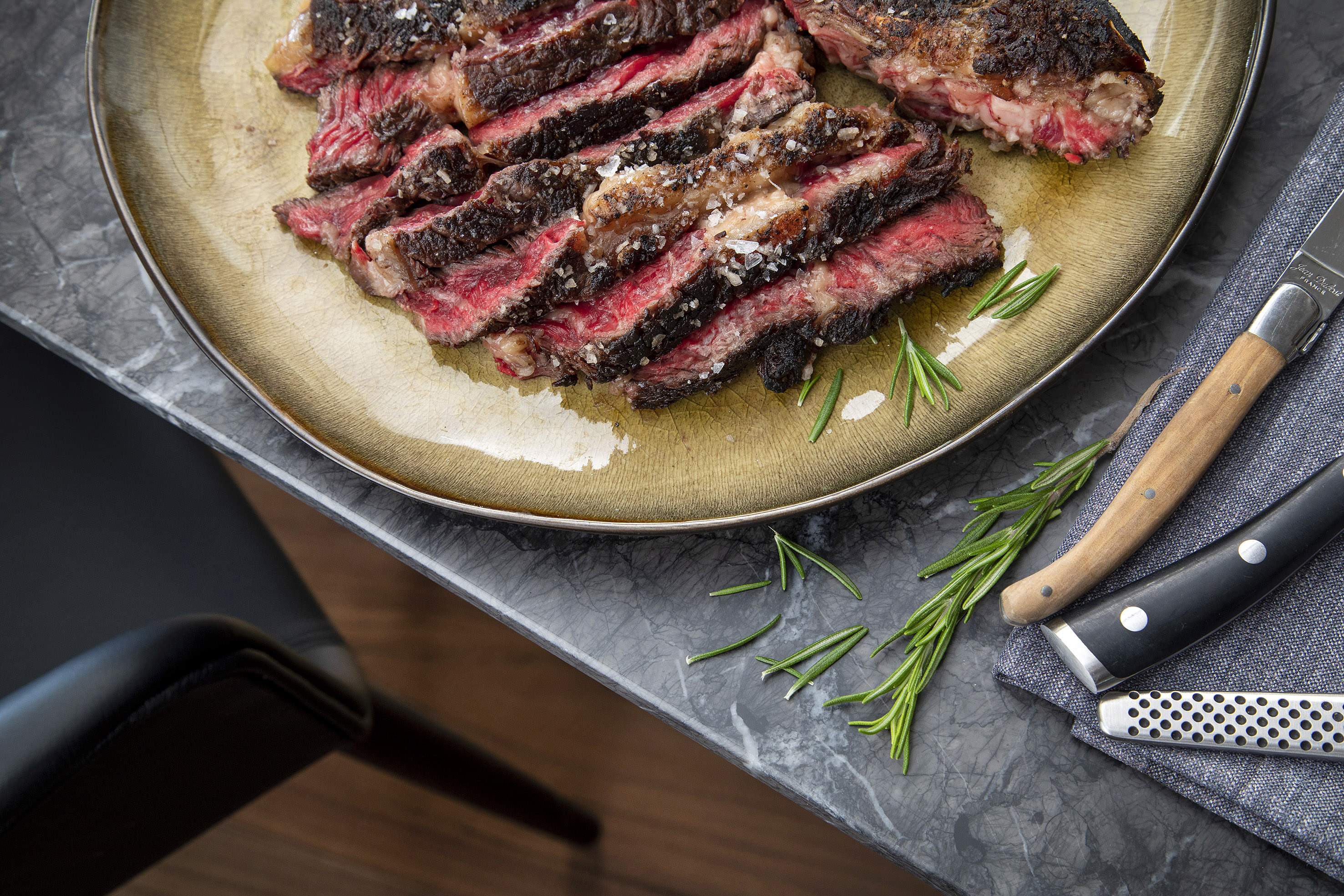 Juicy sliced ribeye steak with flaky salt and fresh rosemary garnish.