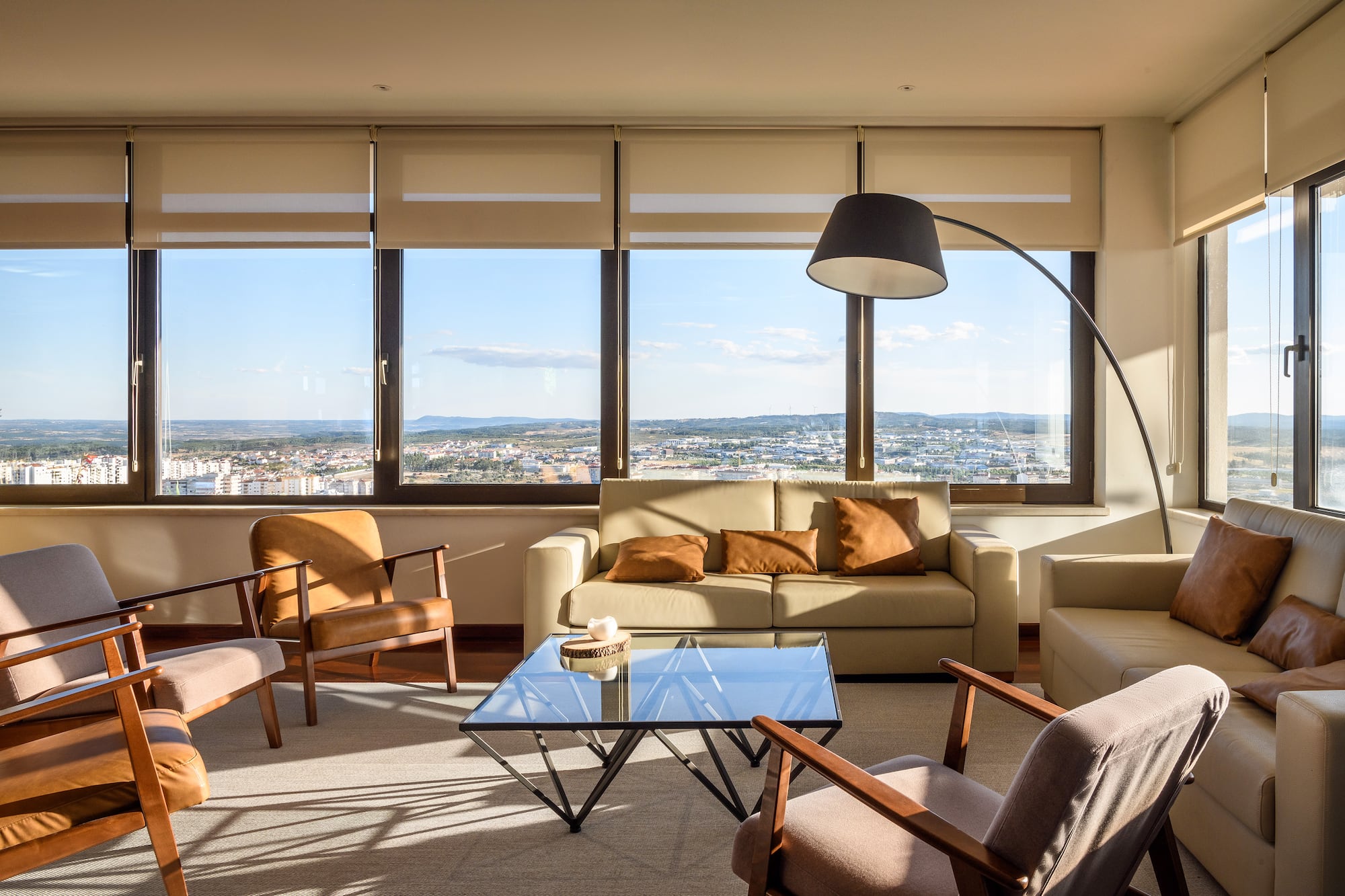 Sunlit living room with city view, modern beige furniture, and large windows.