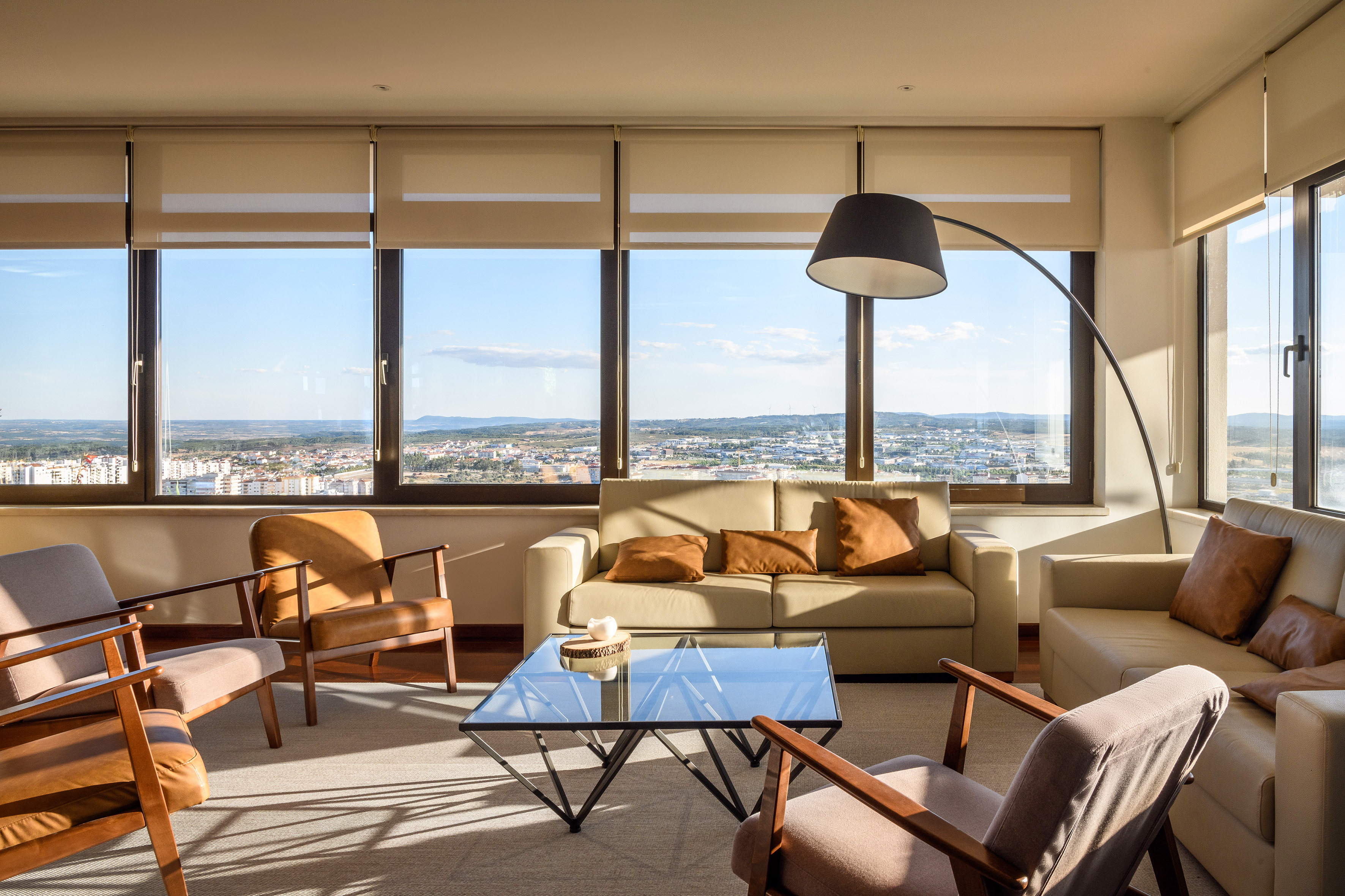 Sunlit living room with city view, modern beige furniture, and large windows.