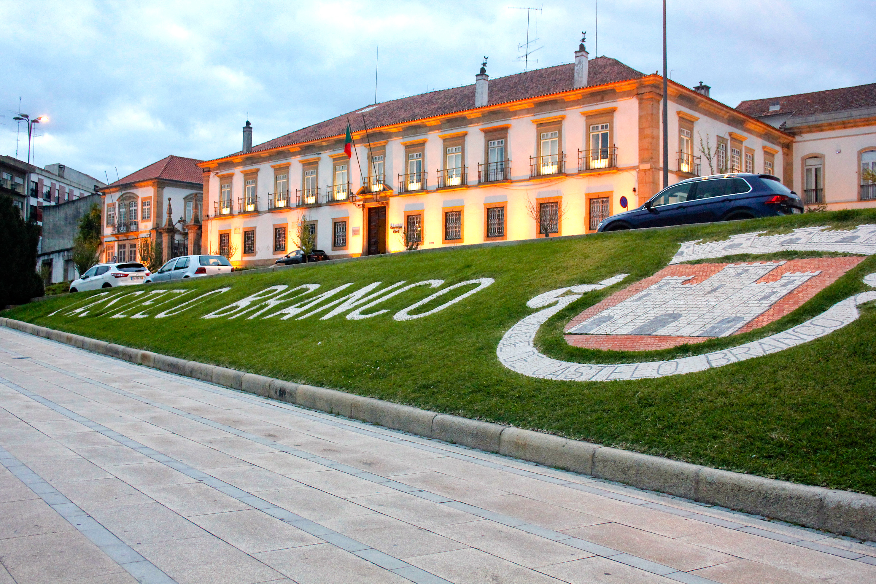Castelo Branco illuminated building at dusk, city name & emblem on grass.