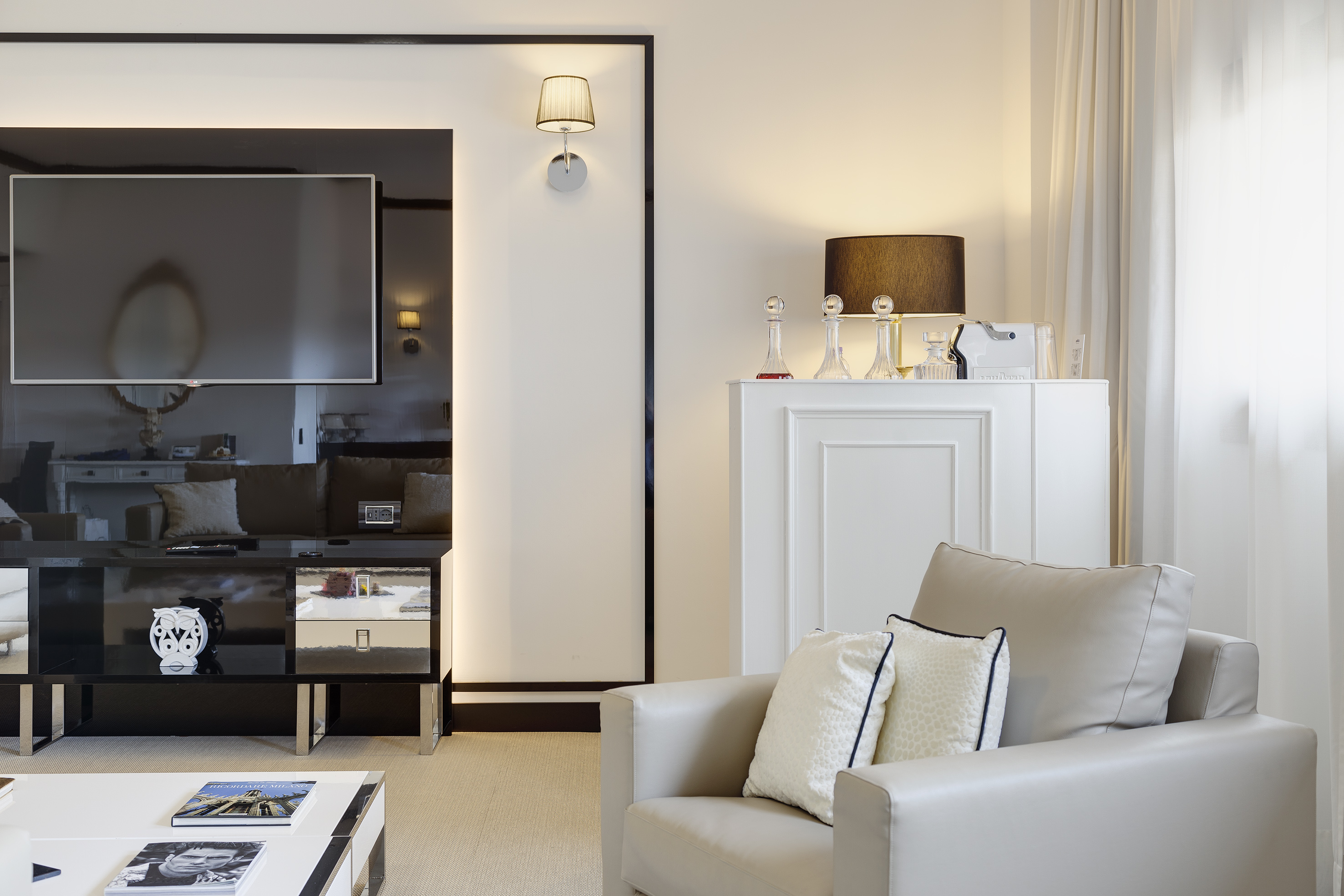 Modern living room with beige armchair, large TV, and minimalist white decor.