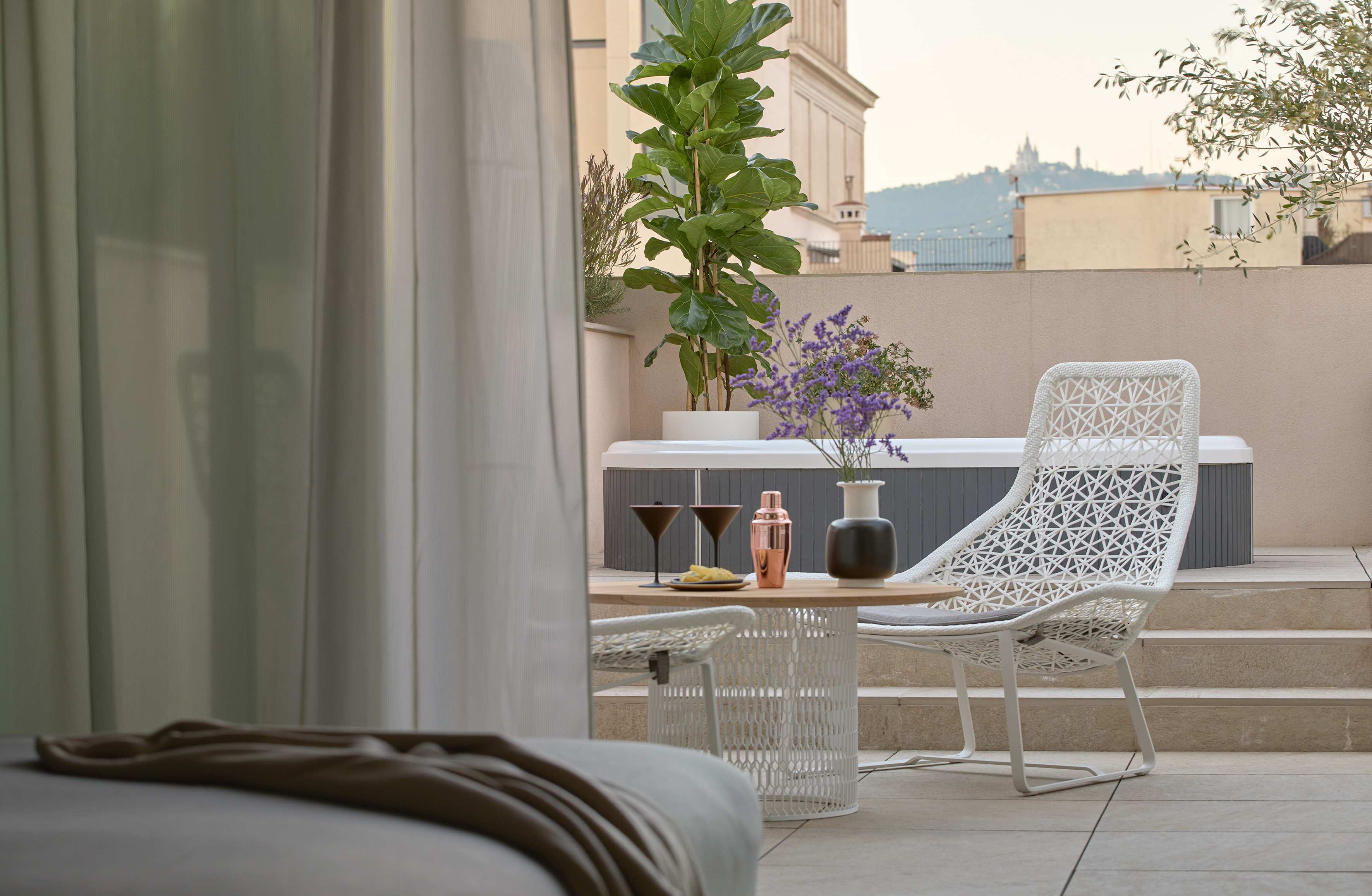 Rooftop terrace with hot tub, white woven furniture, cocktails, city background.