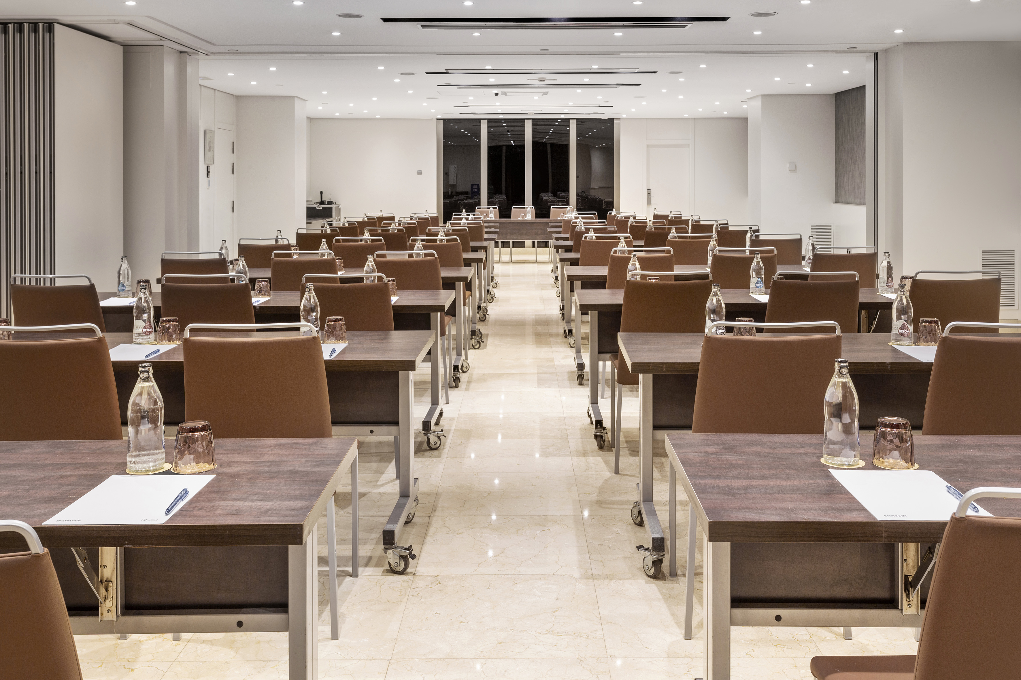 Modern conference room with classroom-style tables, brown chairs, and water bottles.