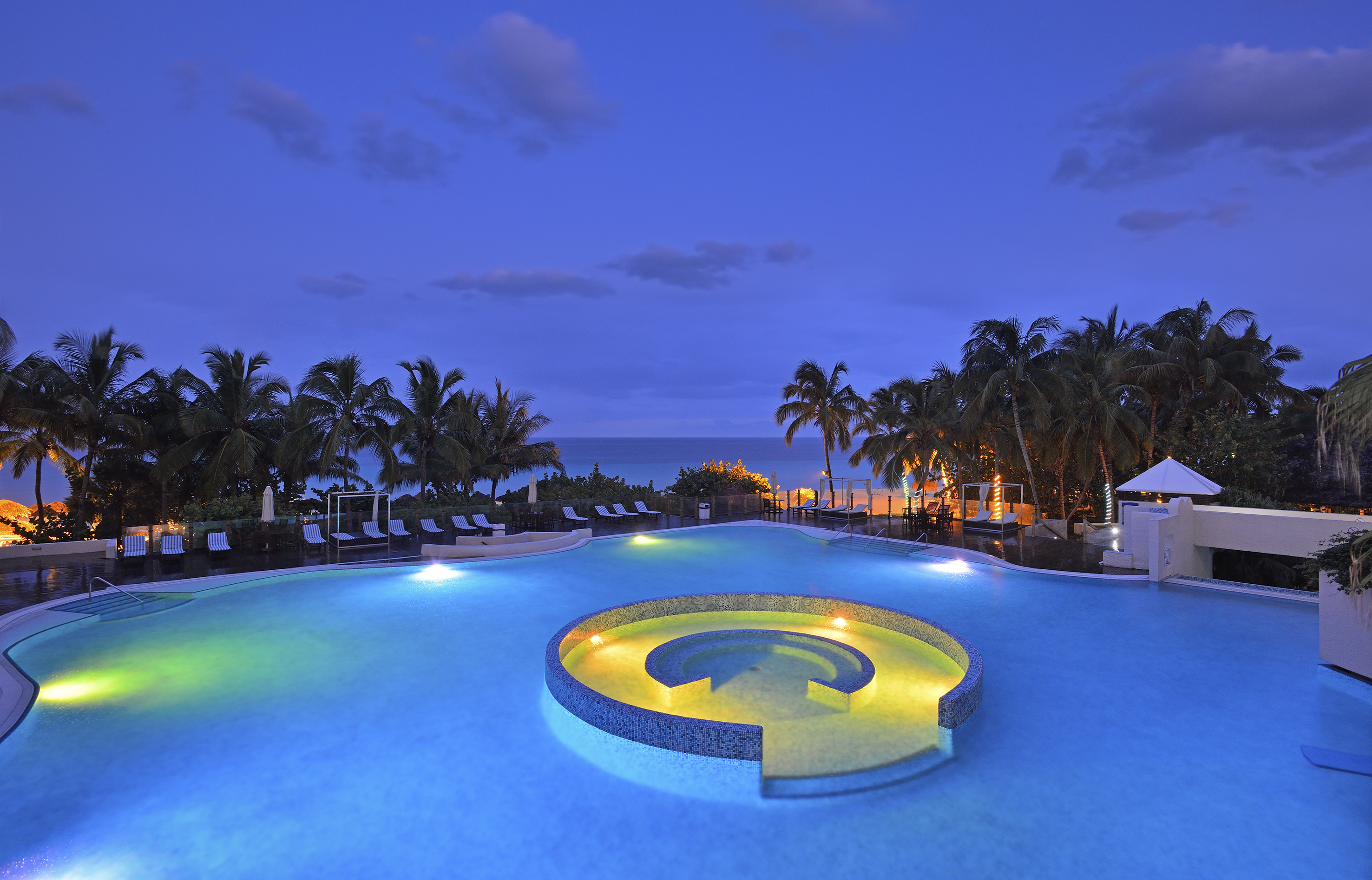 a pool with a circular pool with lights and palm trees