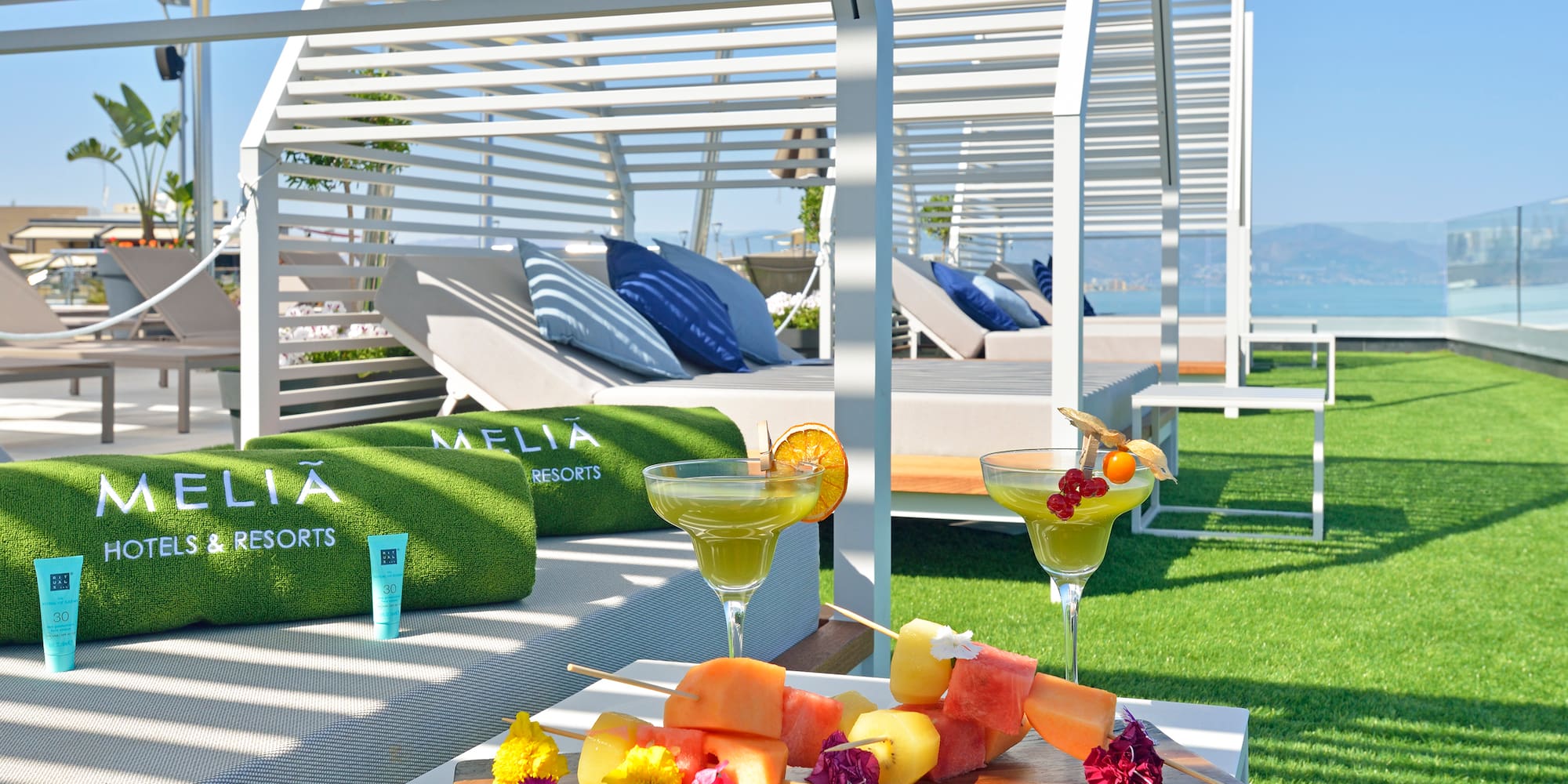 a tray of fruit and drinks on a table by a beach