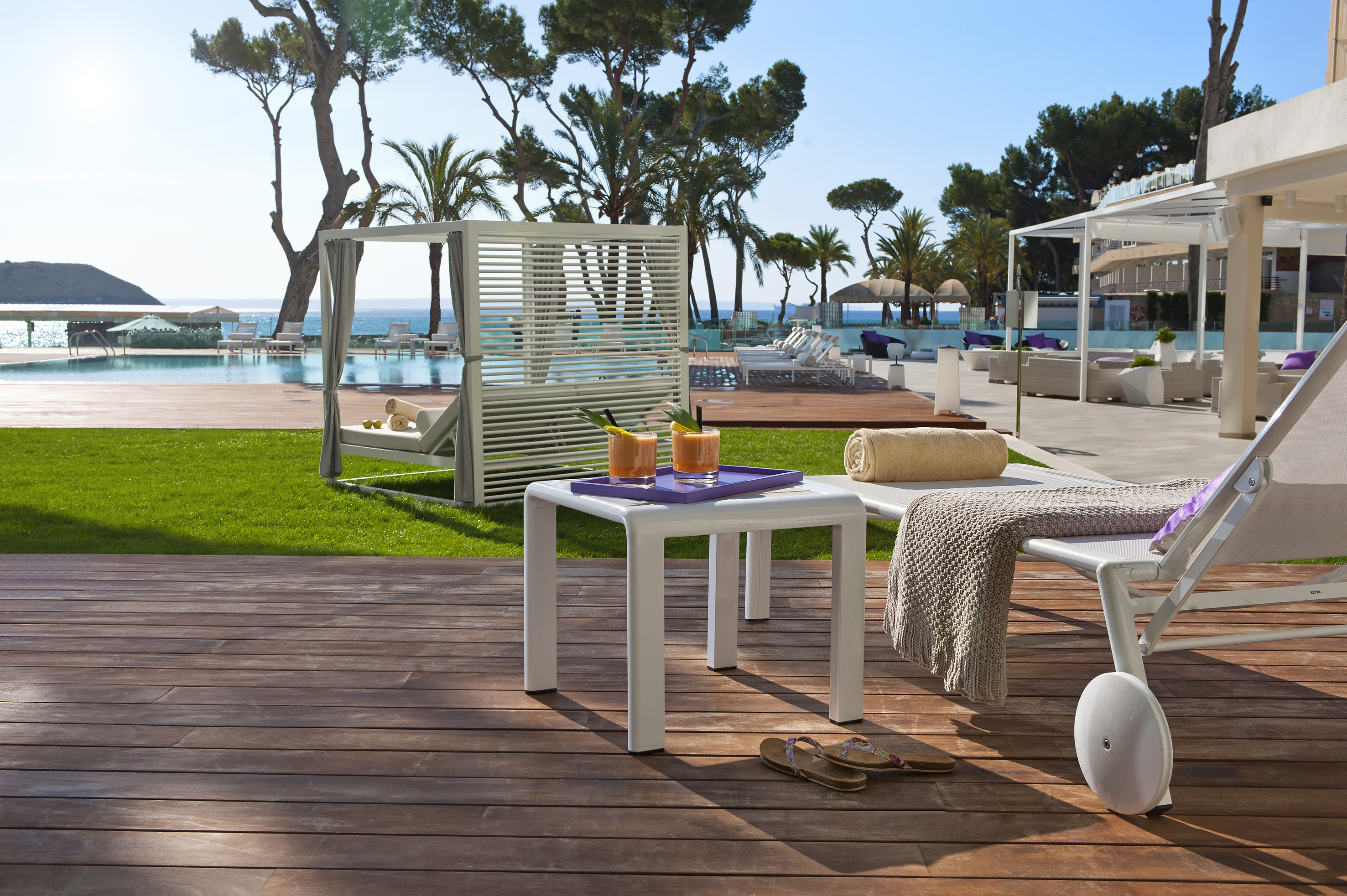 Hotel poolside lounge with cocktails, daybed, sun loungers, and sea view.