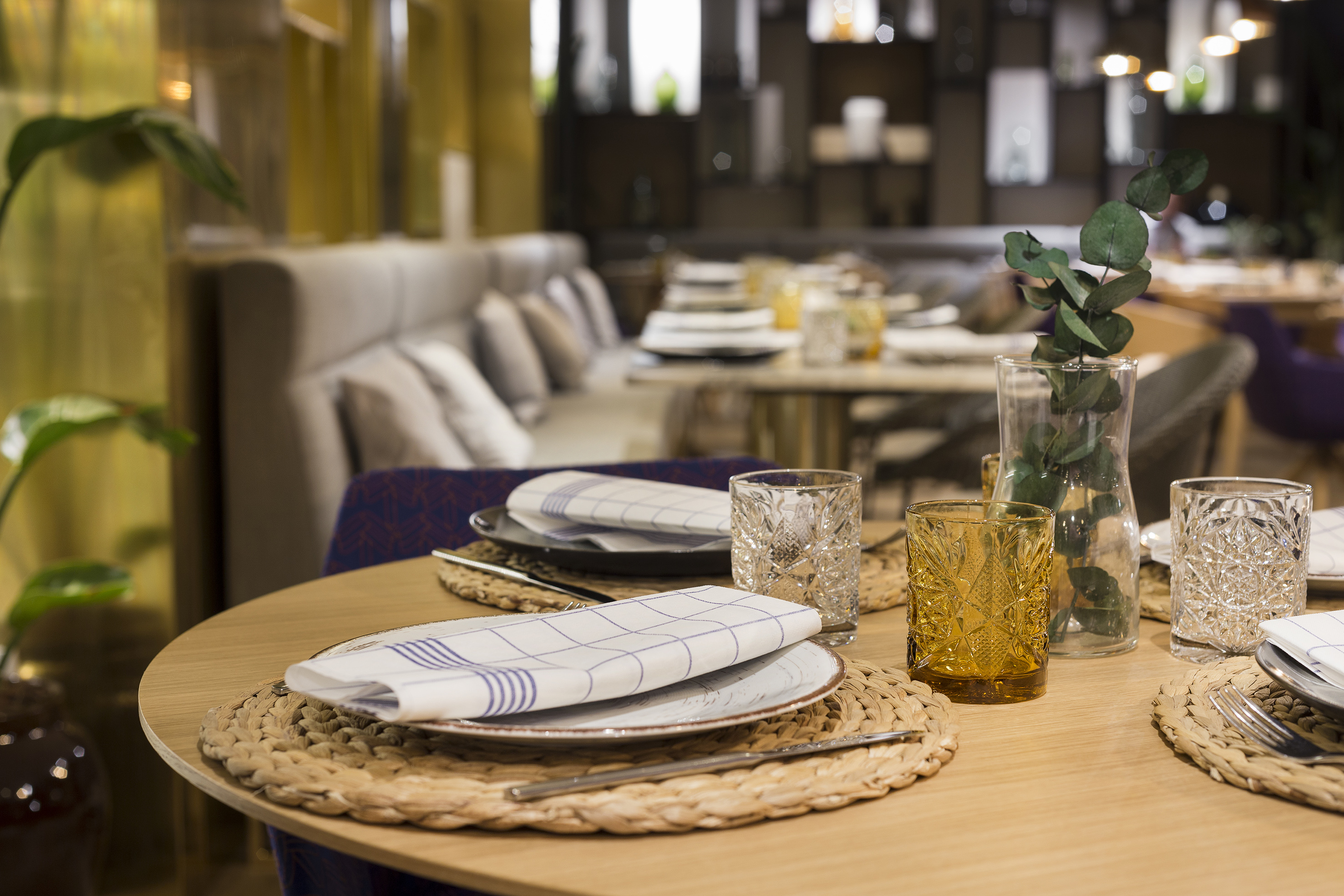 Modern restaurant dining table set with placemats, patterned glasses, and eucalyptus.
