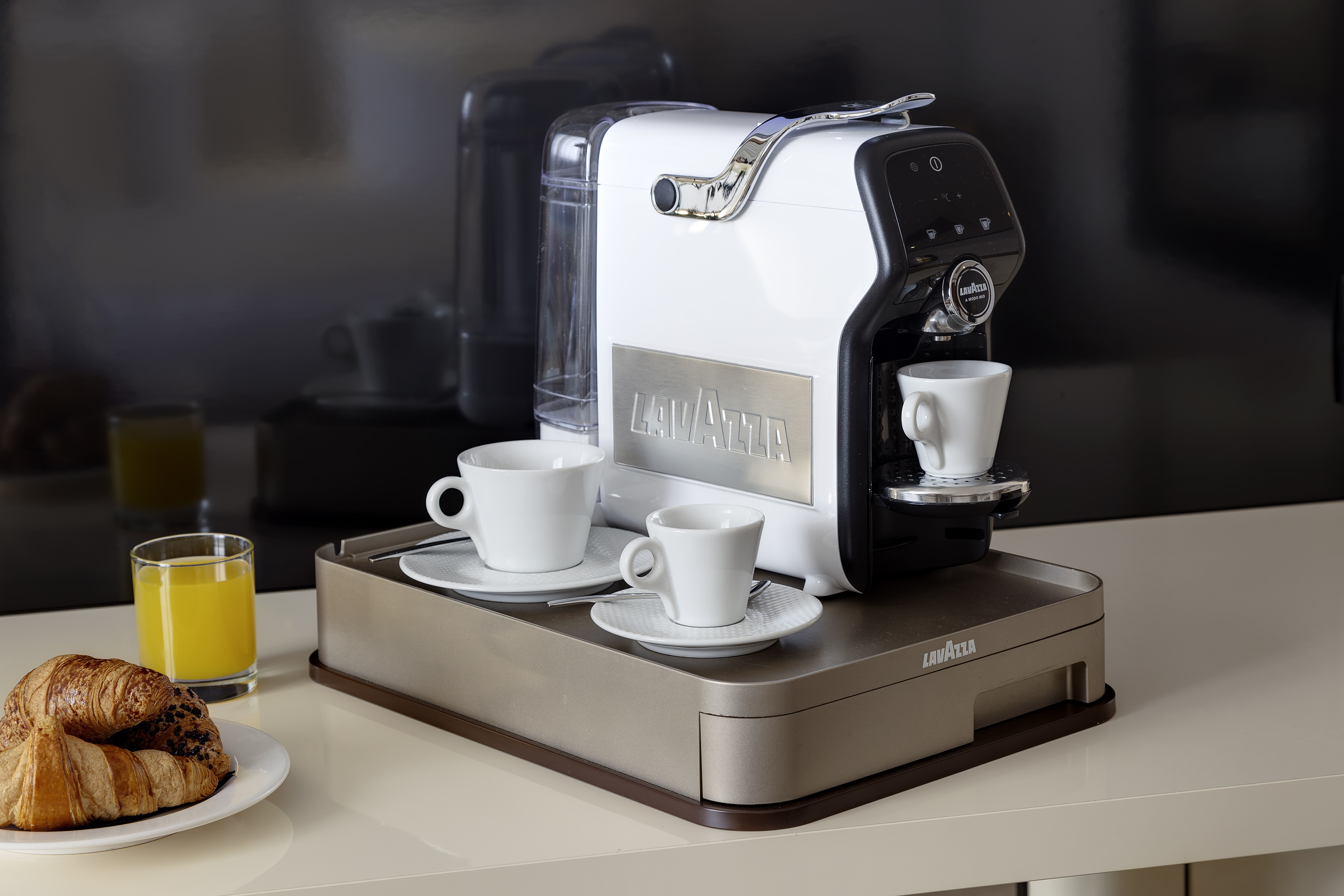 White Lavazza espresso machine with coffee cups, croissants, and orange juice.