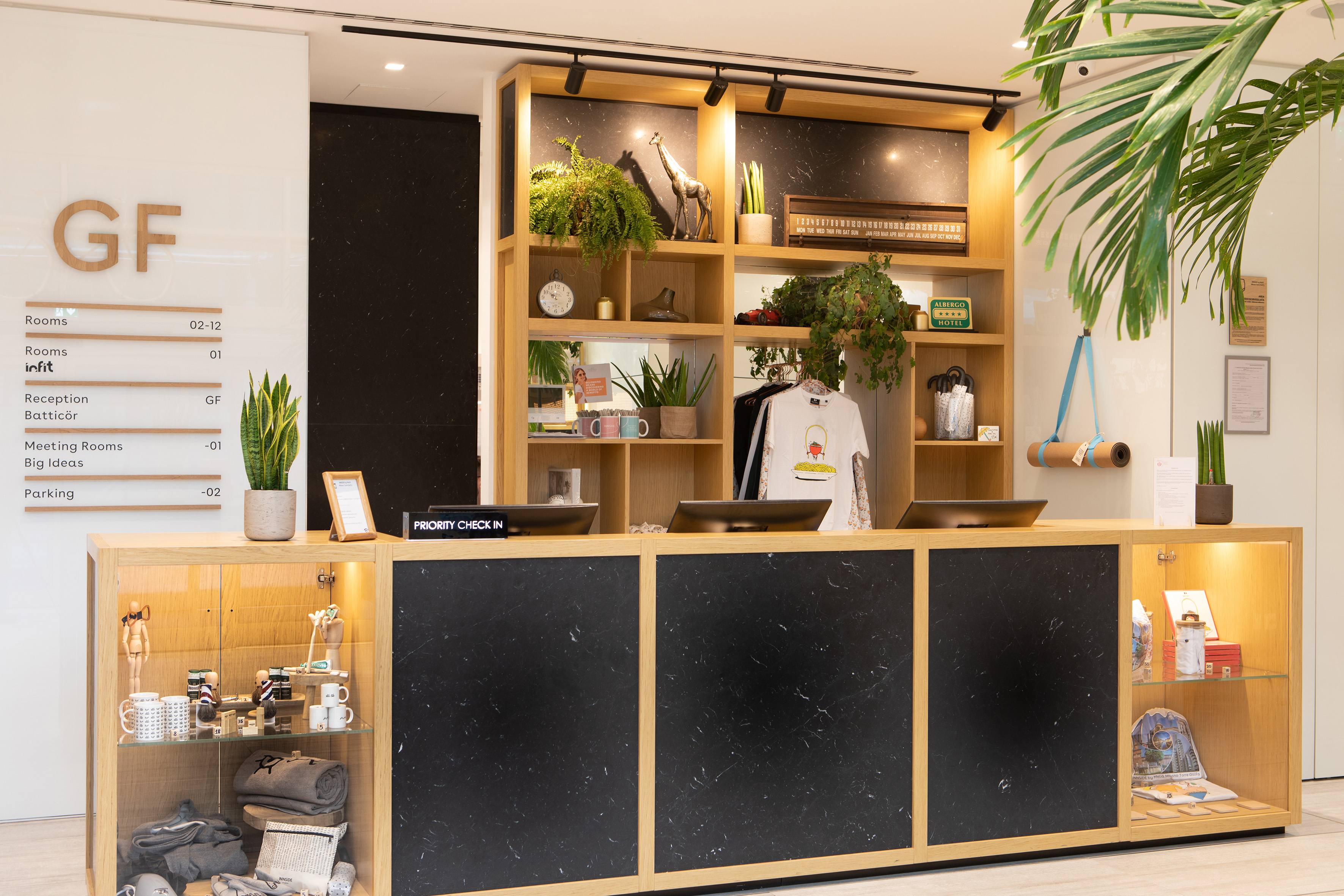 Modern hotel reception desk with green plants and "Priority Check In" sign.