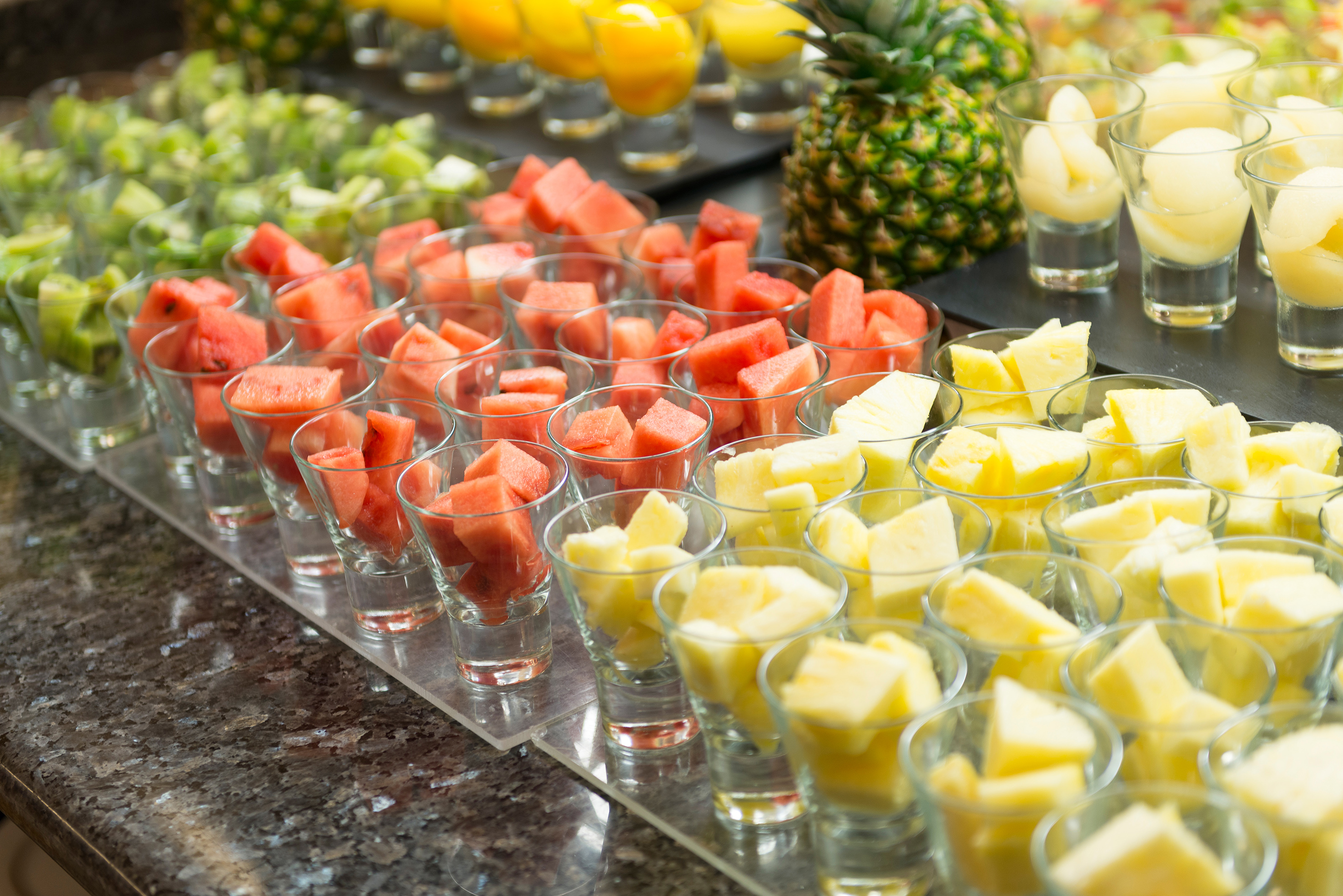 Fresh chopped watermelon, pineapple, and kiwi in glasses at a fruit buffet.