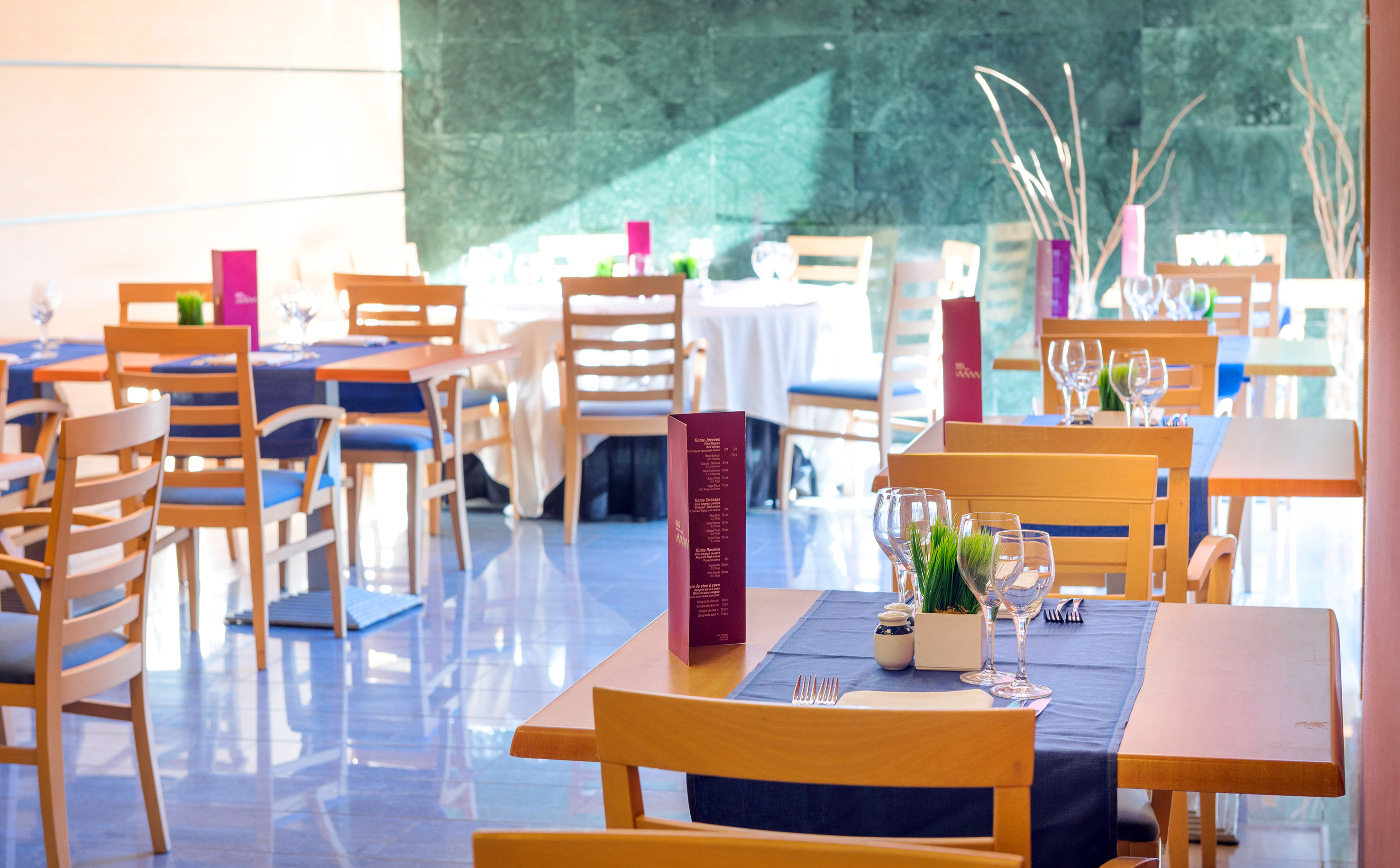 Bright modern restaurant interior with blue table settings and wooden chairs.