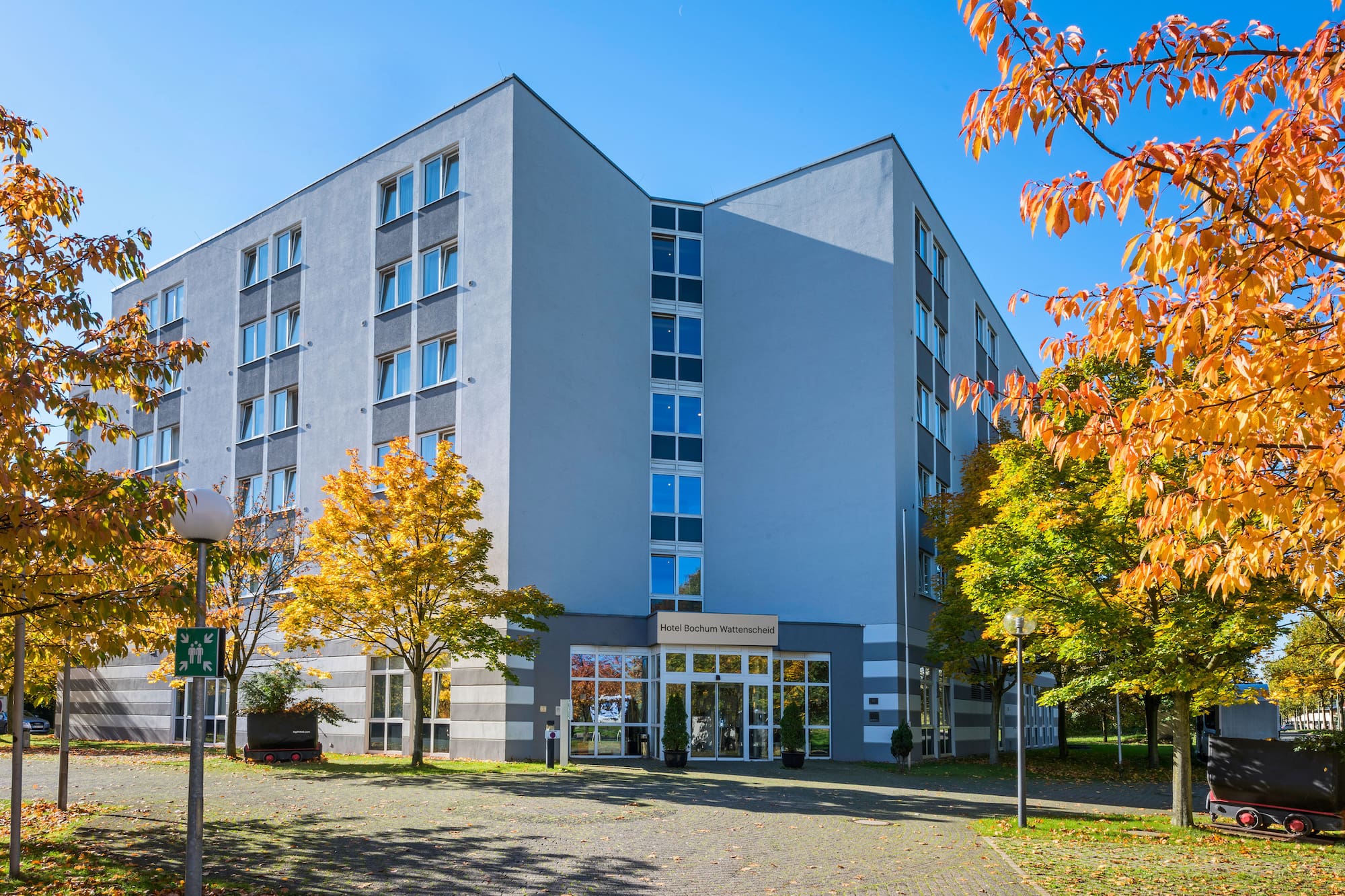 Hotel Bochum Wattenscheid, modern building exterior, vibrant autumn trees.