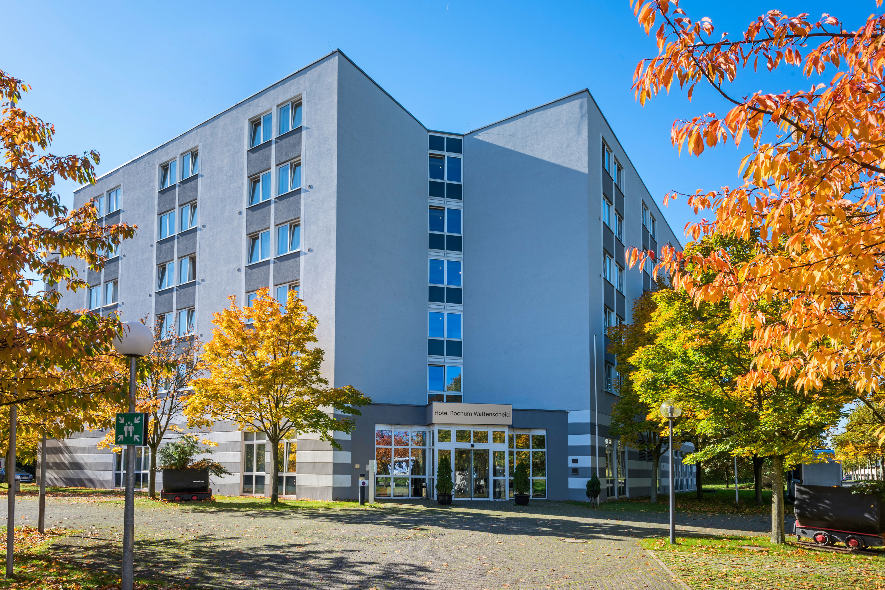 Hotel Bochum Wattenscheid, modern building exterior, vibrant autumn trees.