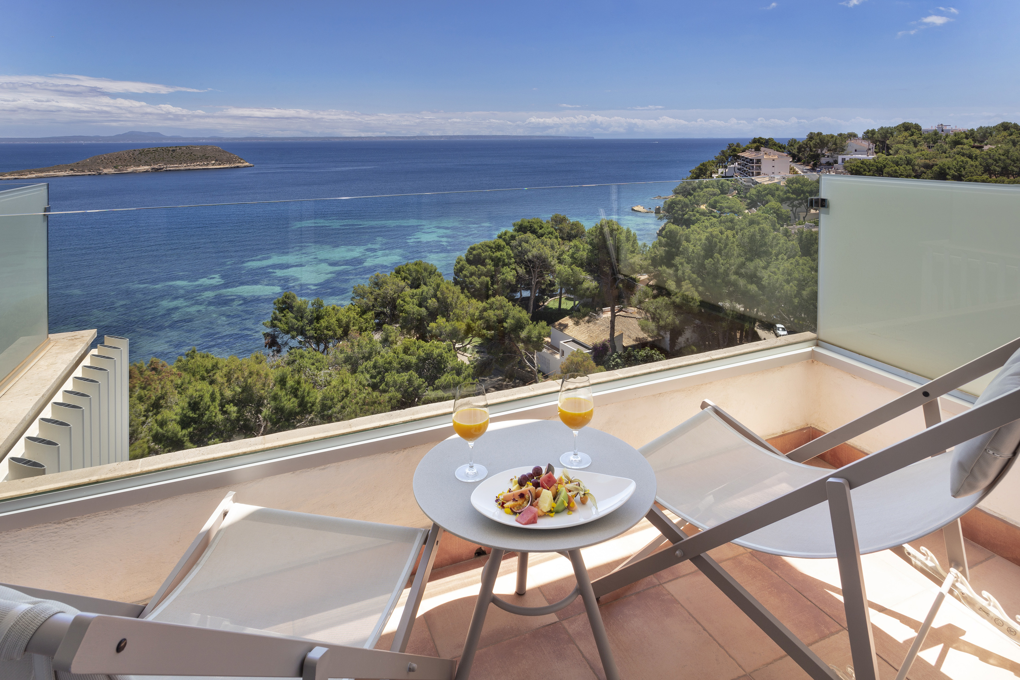 Sunny balcony with fruit salad, orange juice, and panoramic sea view.
